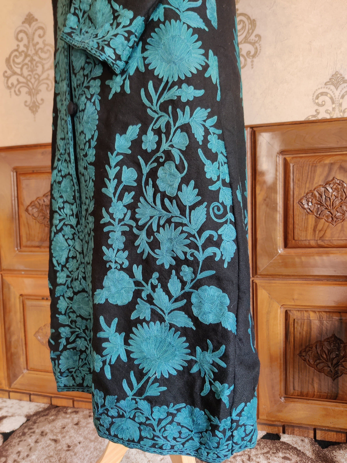 Close-up of the black jacket’s lower front, with turquoise Aari floral vines beside a dense embroidered opening and hem border.