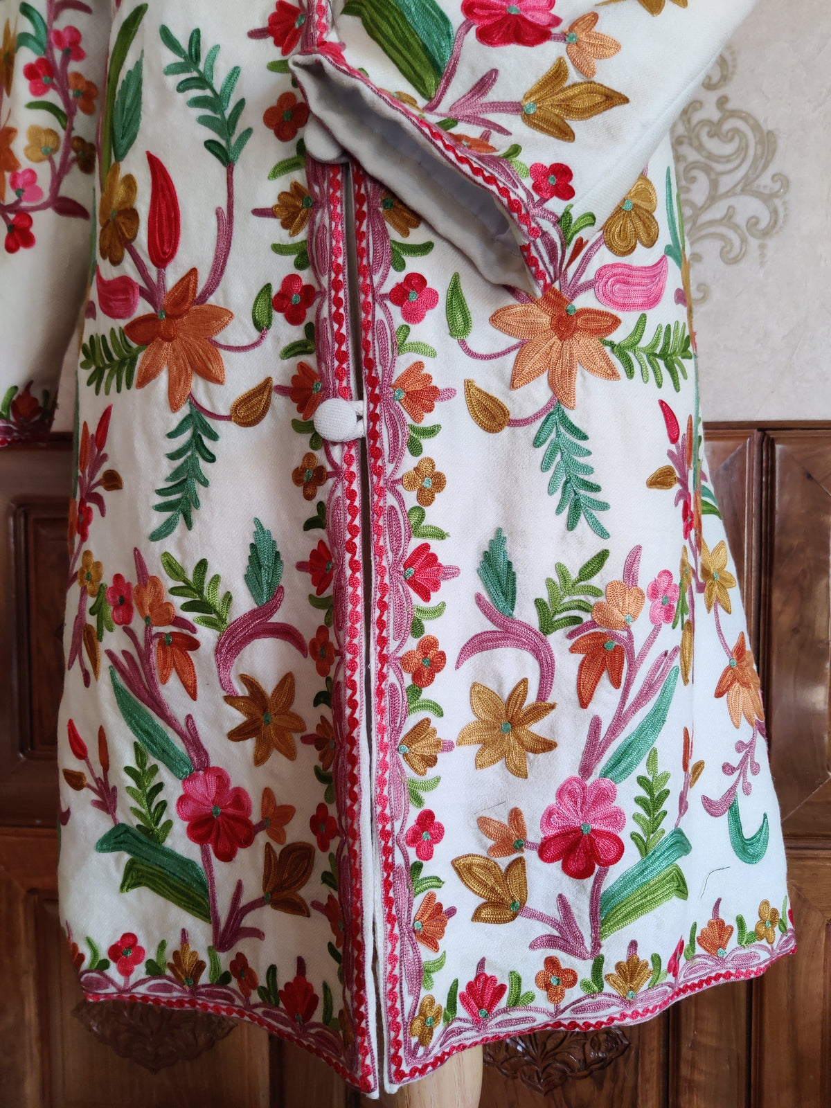 Lower front of a white Aari jacket with multicoloured floral vines and a small red flower border along the hem