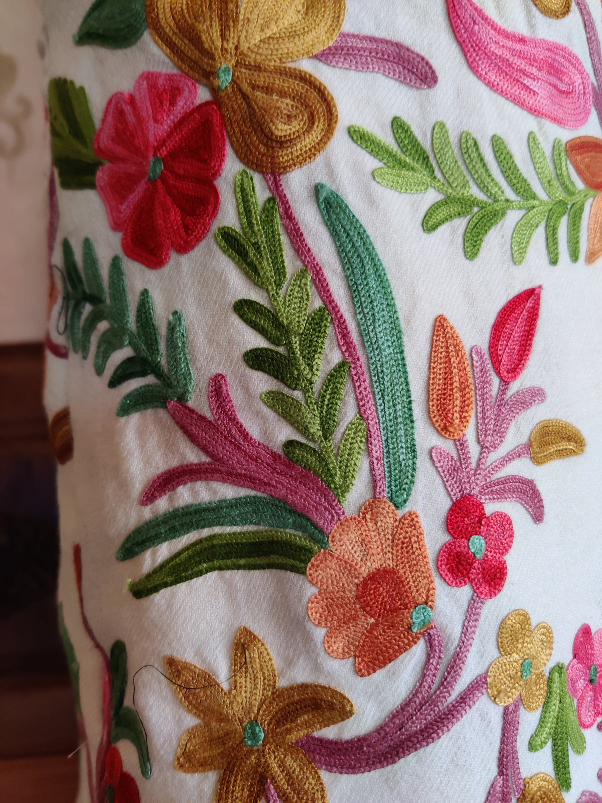 Close-up of red, peach and ochre Aari flowers with green and teal leaves on curling pink stems against white