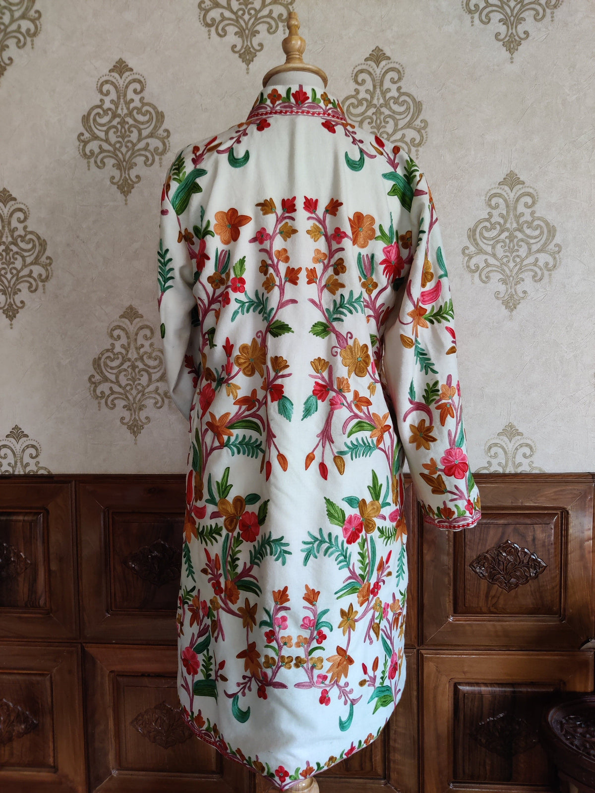 Full back view of a long white Aari jacket, showing colourful flower sprays, green leaves and a narrow floral hem