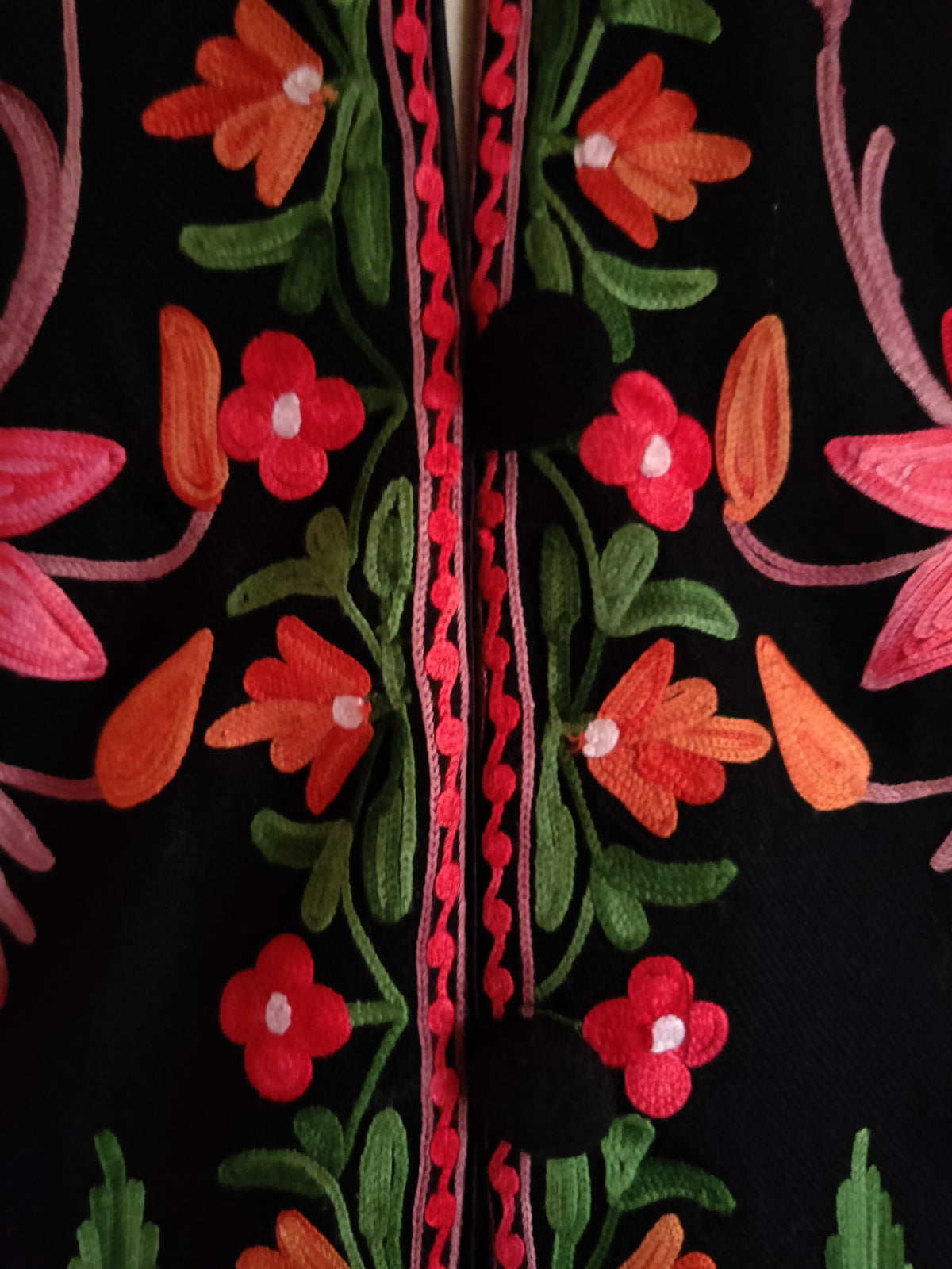 Close-up of black buttons beside the jacket's narrow pink-edged border of orange and red Aari flowers