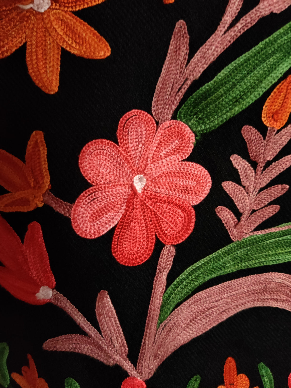 Macro view of a pink Aari flower with pale pink stem and green leaves on black jacket fabric