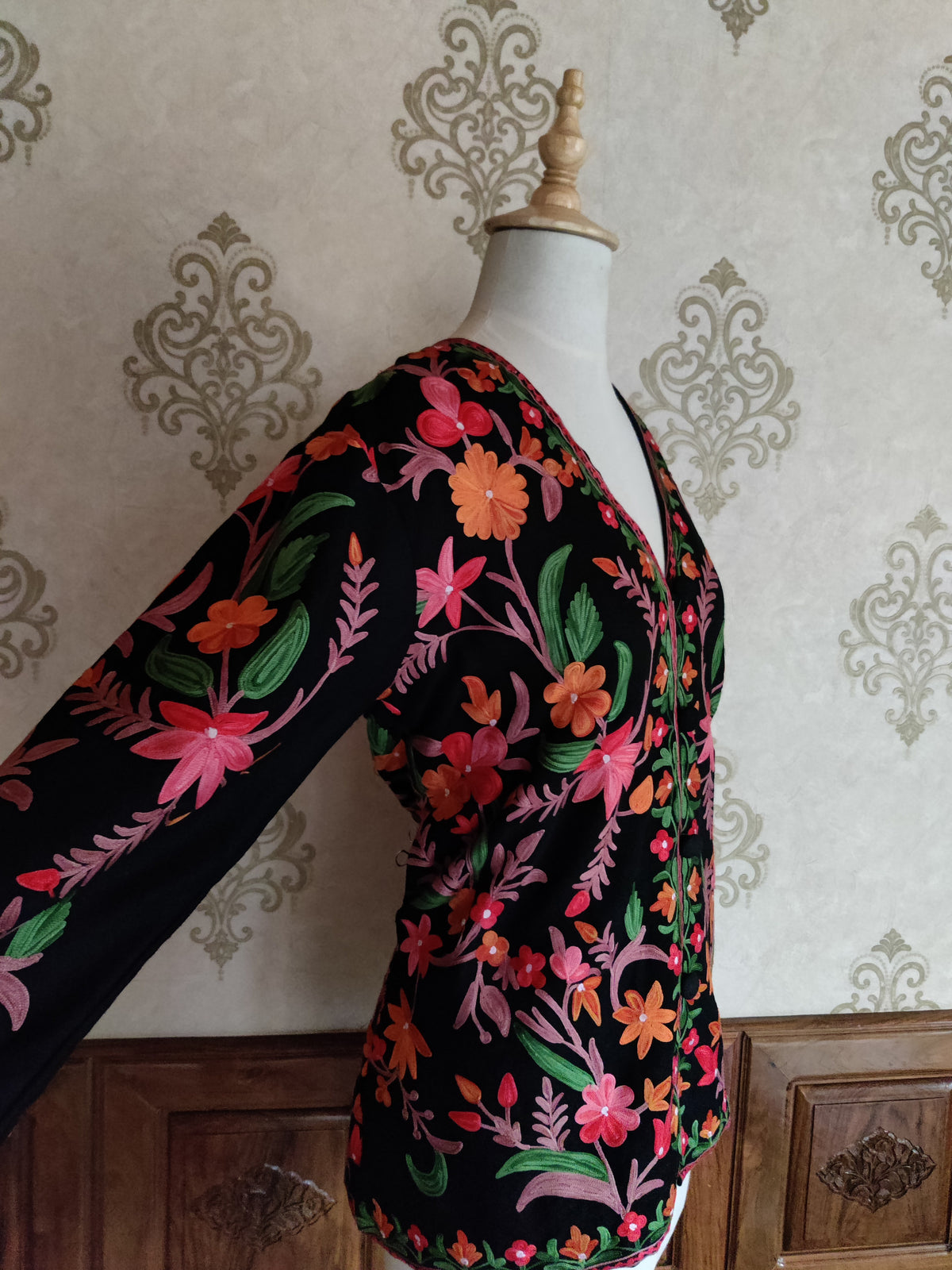 Side-front view of a black short jacket with one sleeve extended, showing pink and orange Aari floral vines
