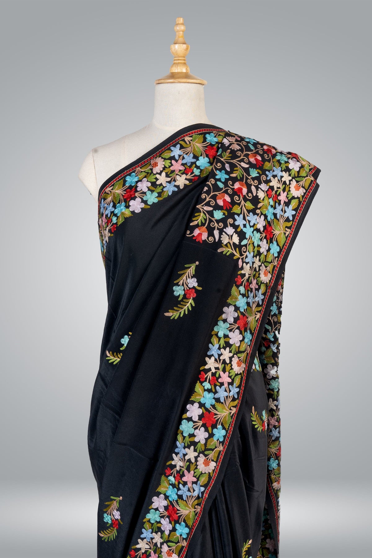 Upper drape of a black crepe saree with dense blue, pink, red and white Aari flowers along the shoulder and diagonal border