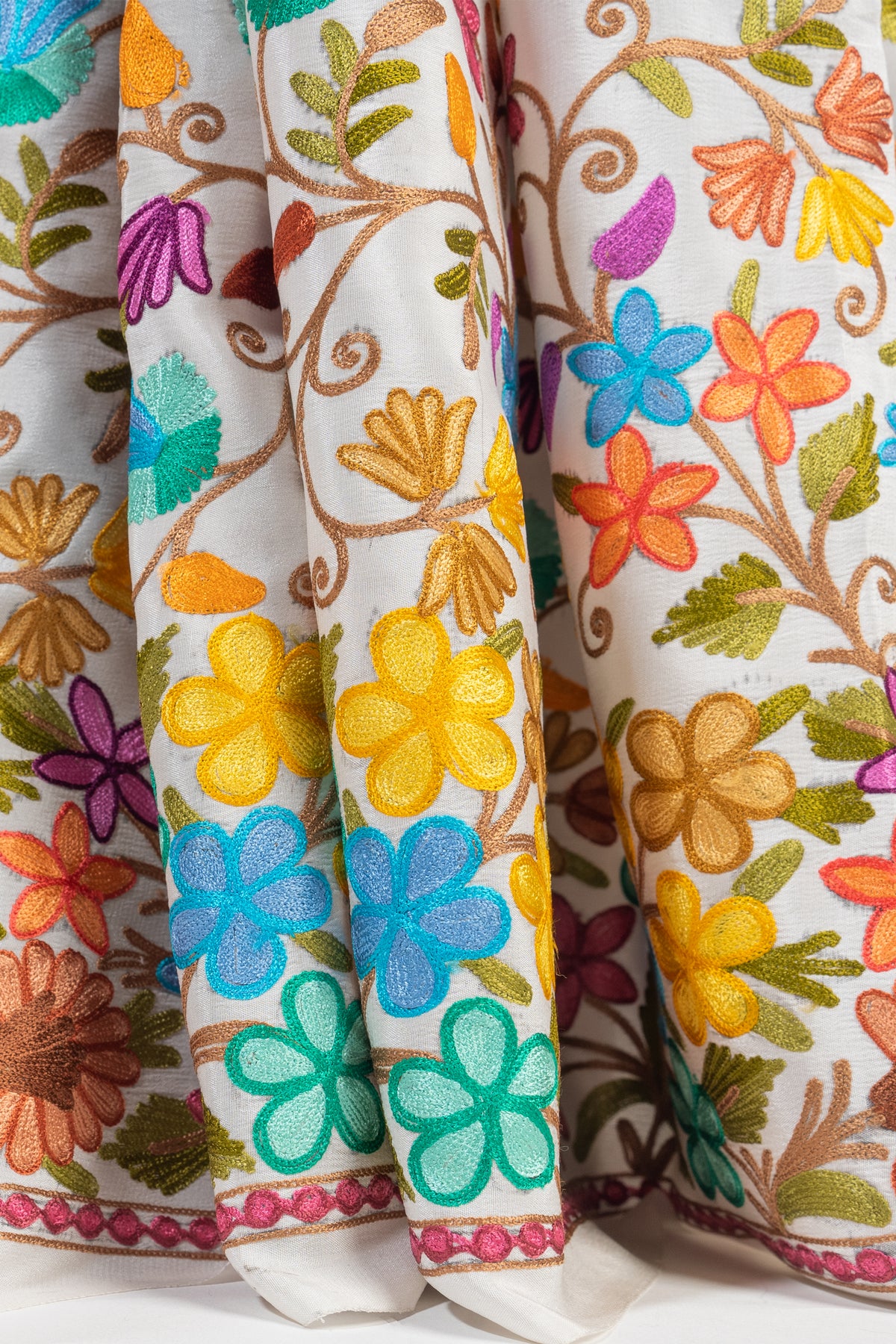 Close-up of pleated white saree fabric with yellow, turquoise, orange and purple flowers and a narrow pink edge.