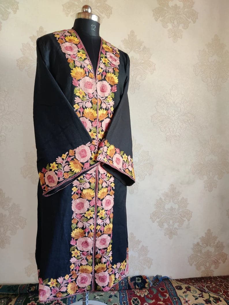 Angled full view of a long black robe with crossed sleeves and broad pink rose and yellow flower borders