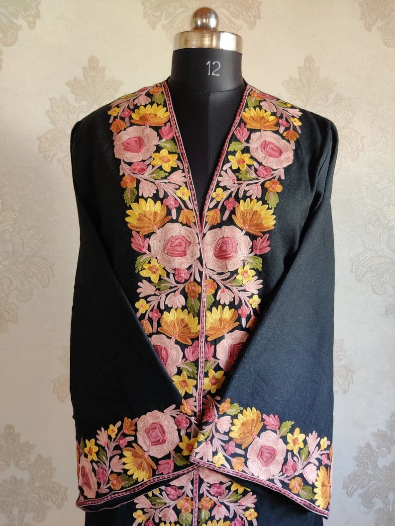 Upper front of a black robe with crossed sleeves and broad pink-and-yellow floral embroidery along the neckline and cuffs