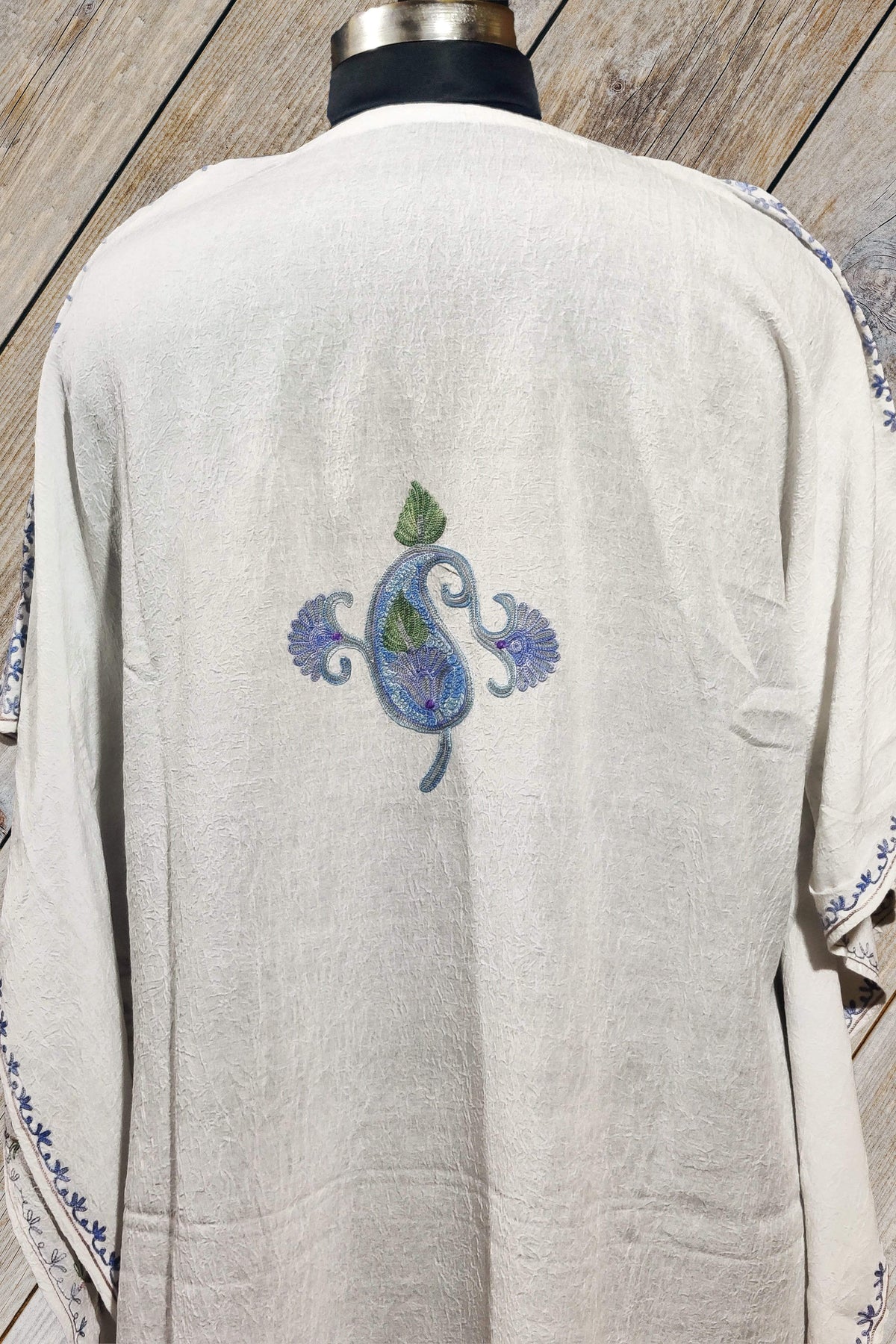 Back detail of a white cotton kaftan, with a single blue-and-green Aari paisley floral motif centred between the shoulders.