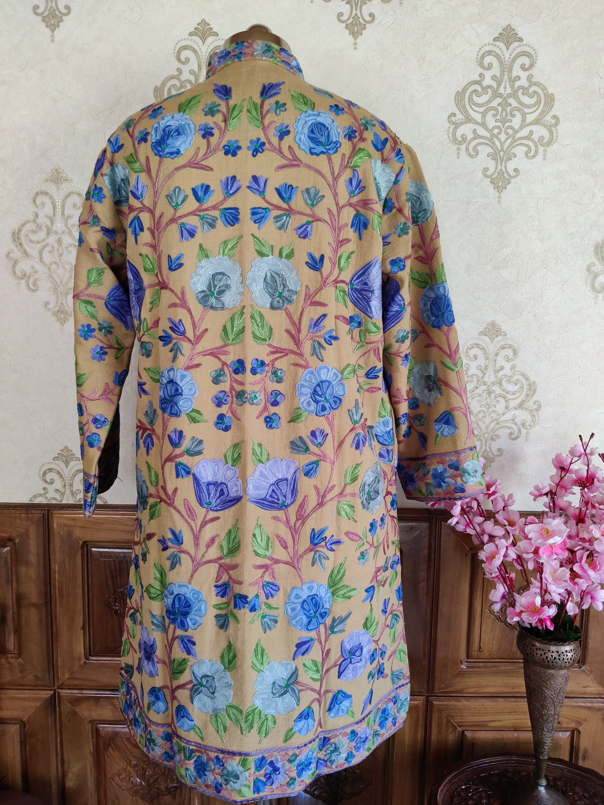 Back of a golden-beige jacket with symmetrical blue and lavender flowers, green leaves and pink branching stems.