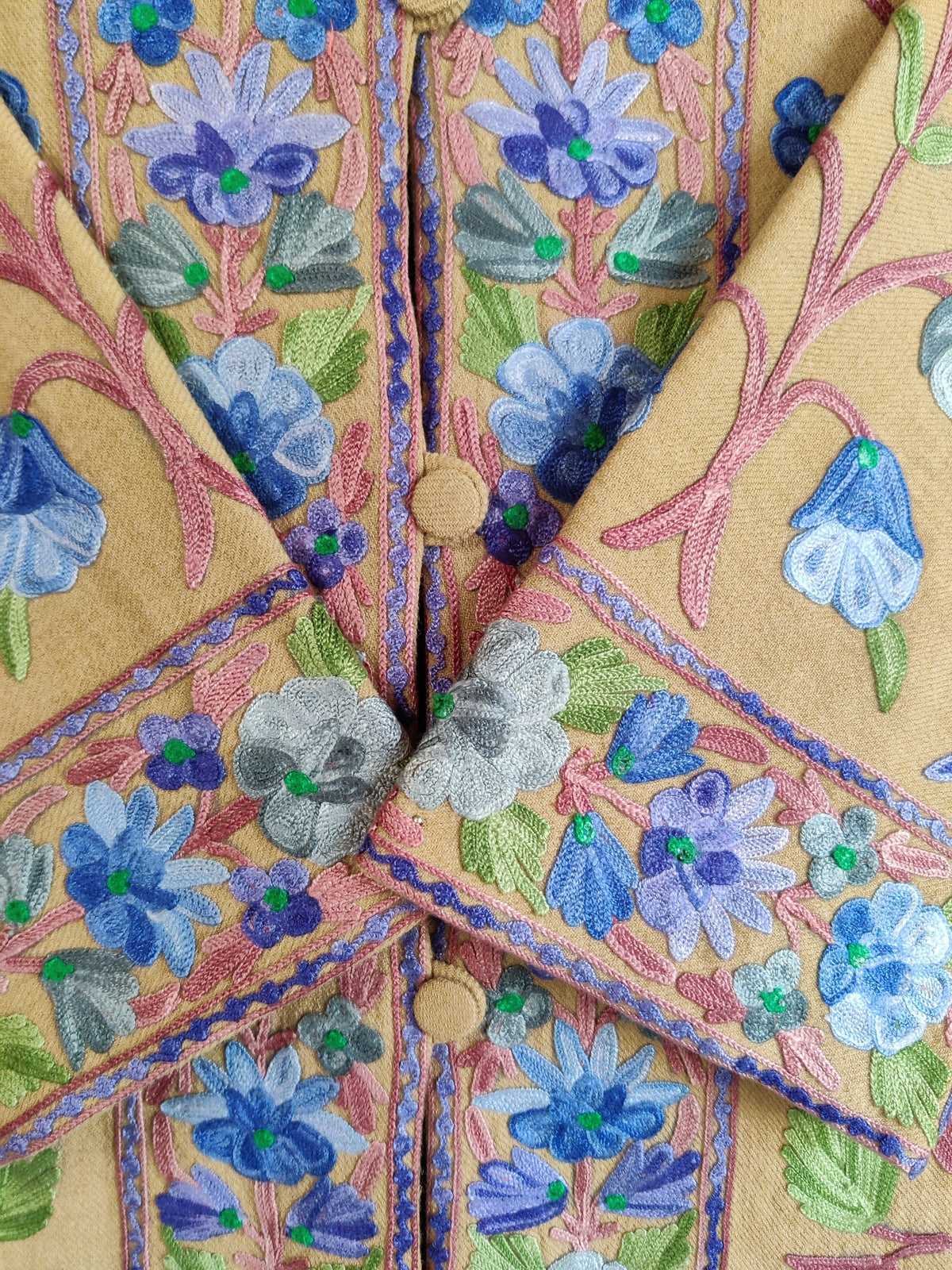 Close-up of the jacket’s crossed cuffs and front buttons, bordered with blue and lavender flowers on golden-beige fabric.