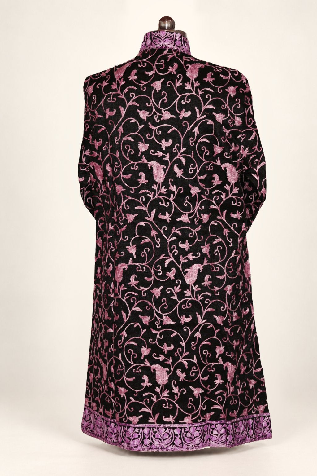 Back of a black long coat on a mannequin, with pink-purple Aari floral vines and dense matching embroidery on the collar and hem.