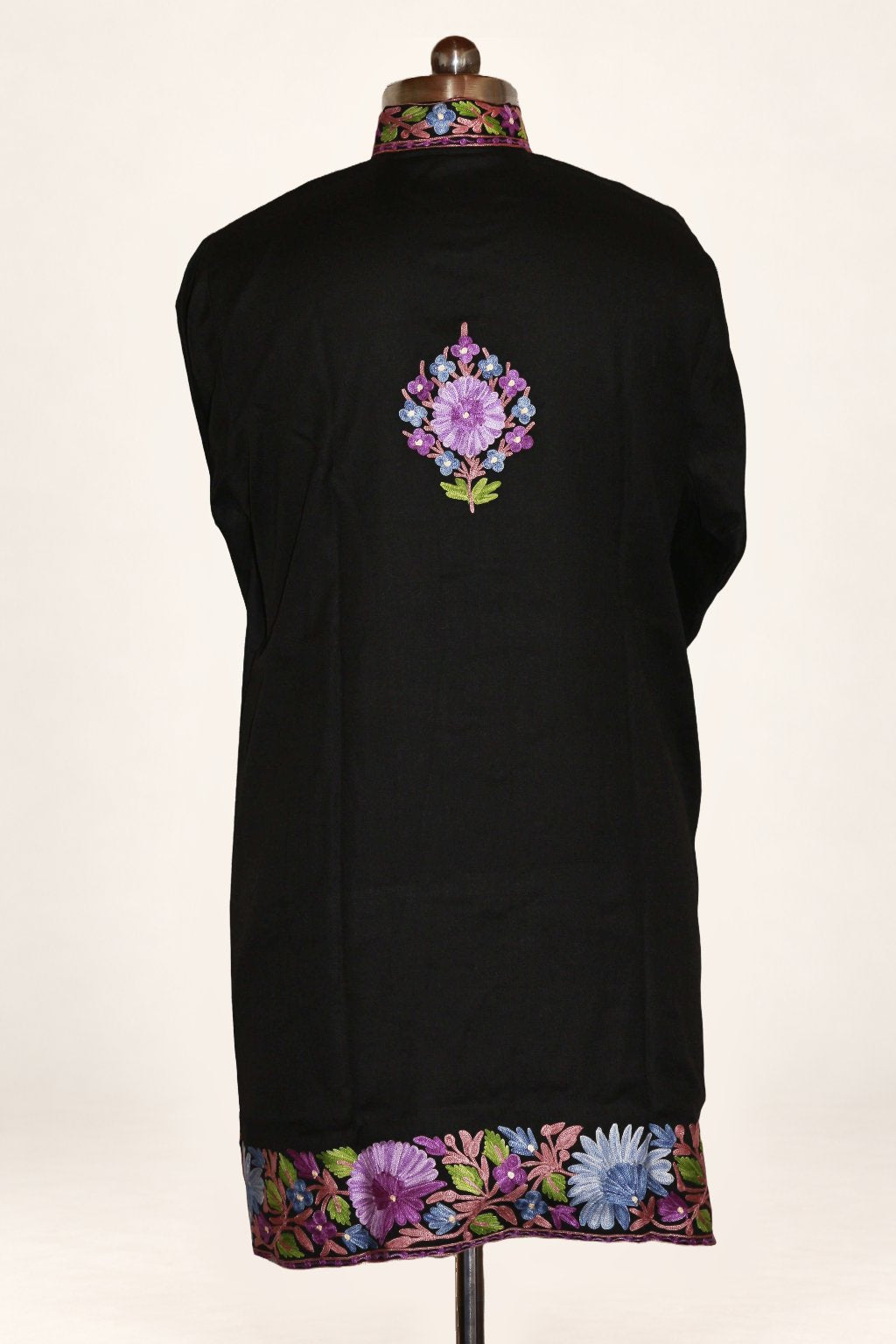 Back of a black jacket on a mannequin, with a small lilac Aari floral motif between the shoulders and multicoloured flowers along the hem.