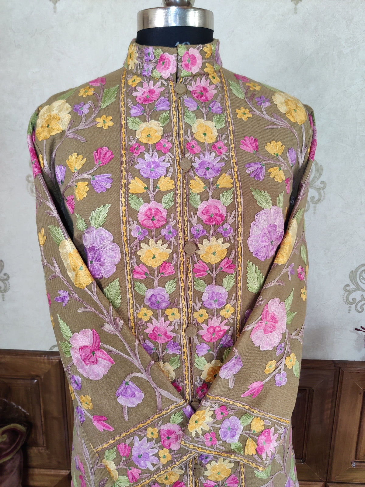 Upper-front close-up of taupe coat with standing collar, crossed cuffs and pink, lilac and yellow Aari floral embroidery