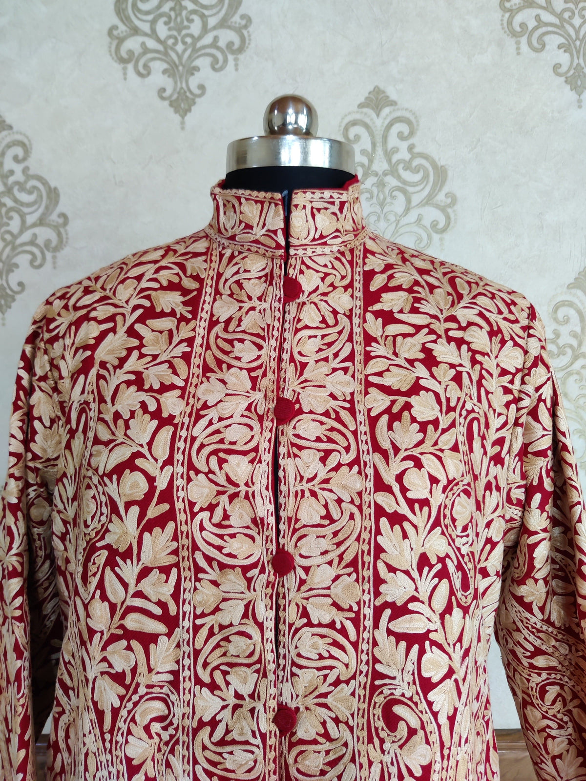 Close-up of the maroon jacket’s stand collar and cream embroidered front panels with paisley and leaf patterns.