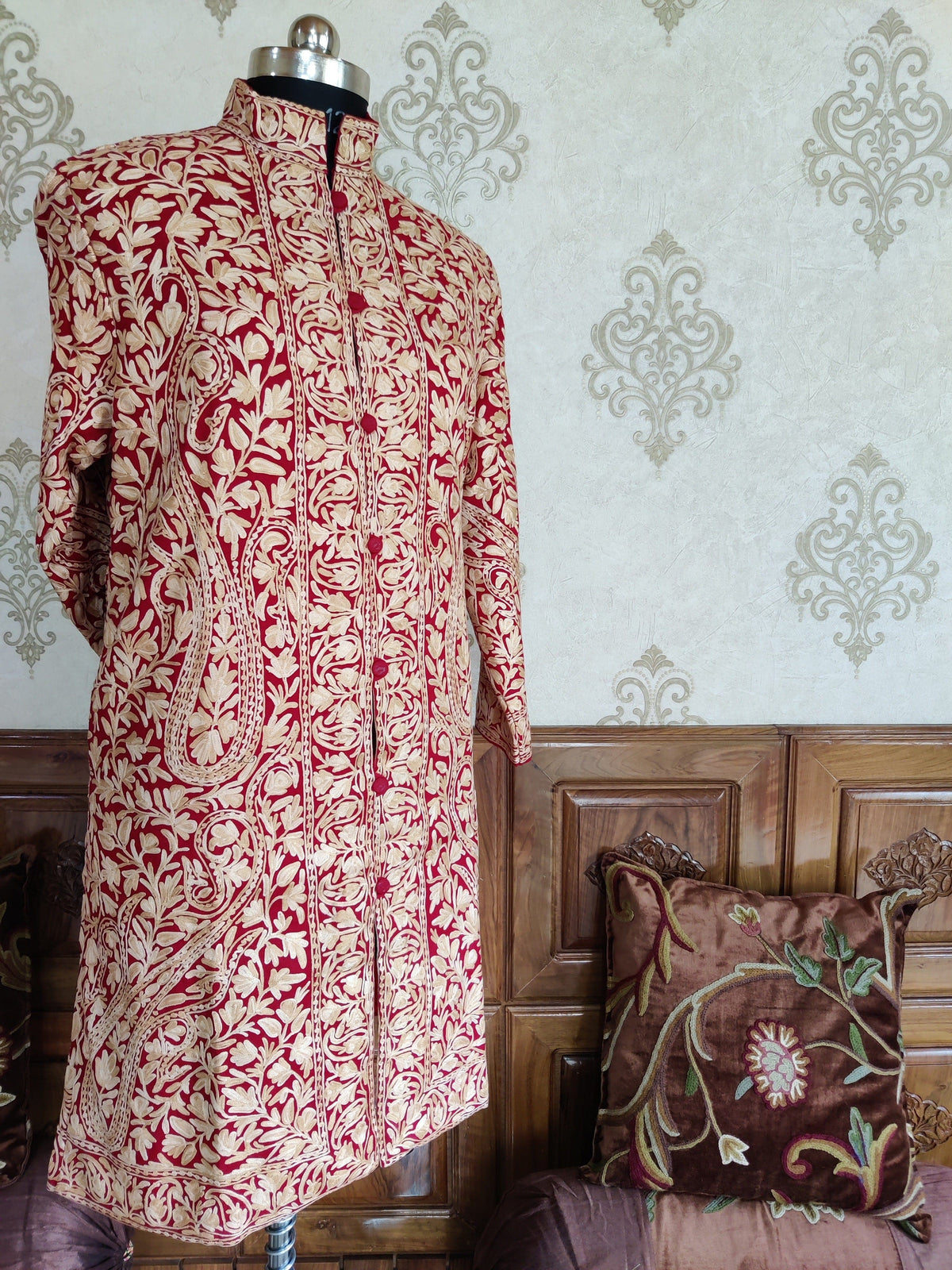 Angled front view of a maroon jacket with cream all-over paisley embroidery, a stand collar and patterned front borders.