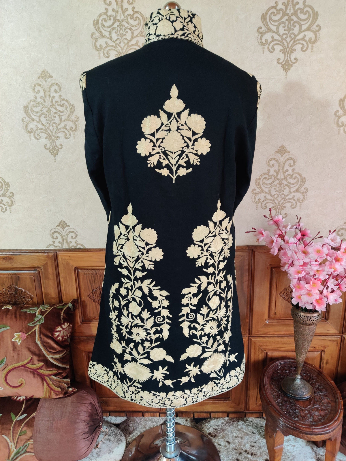 Back view of a black long jacket, with a white floral motif between the shoulders and Aari floral borders around the hem