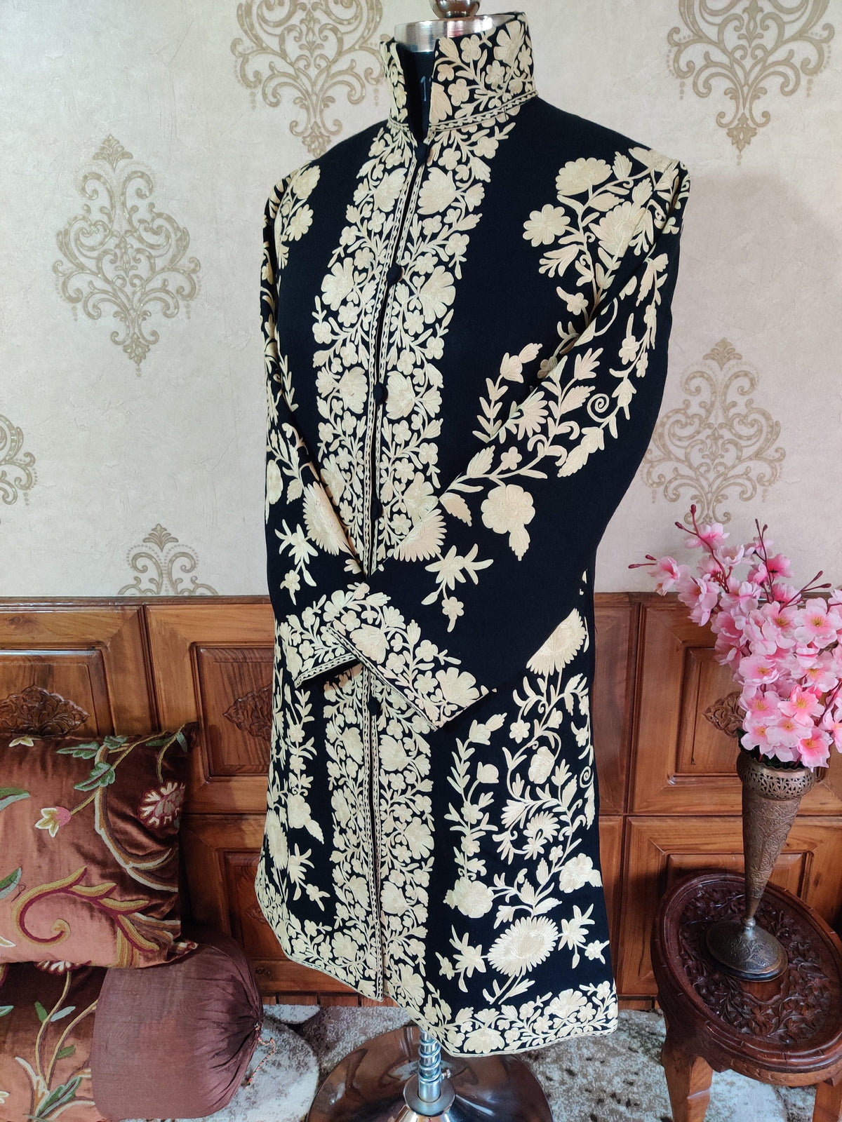 Front three-quarter view of a black long jacket with white Aari floral embroidery, a stand collar and crossed sleeves