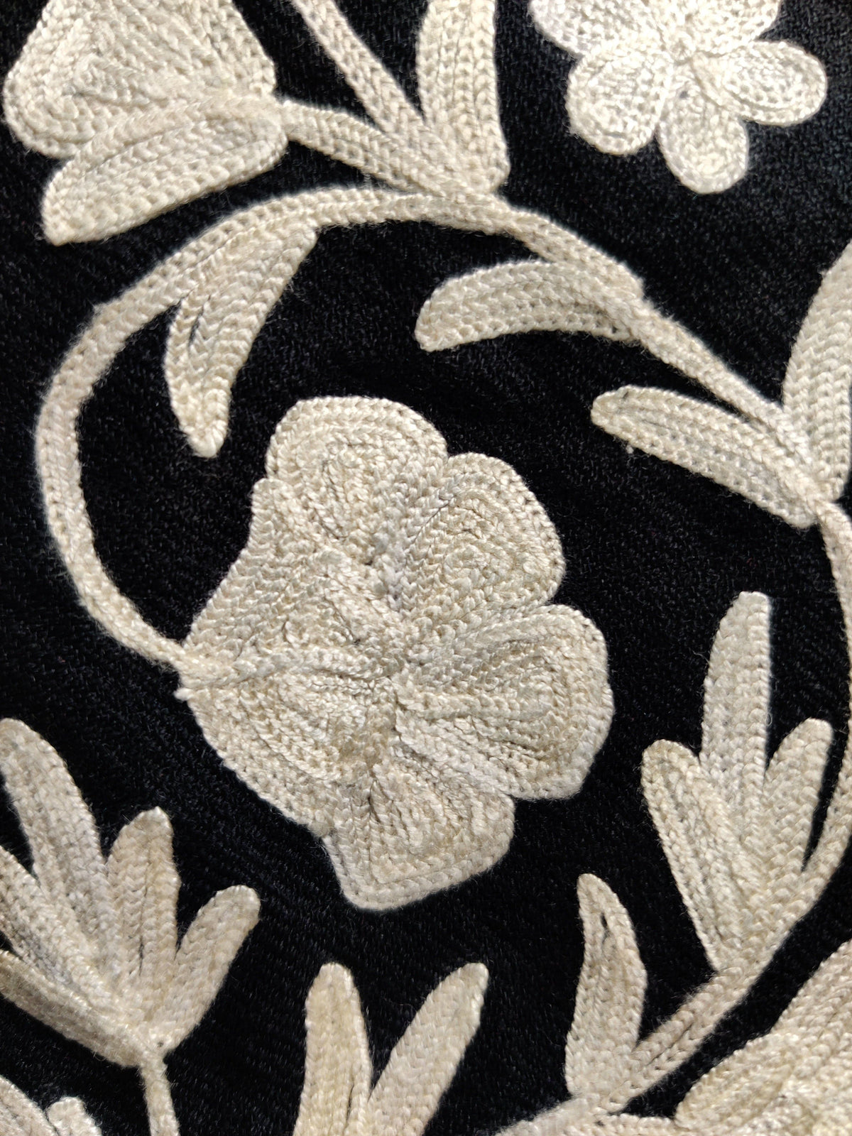Detail of pale floral petals, leaves and stems, showing the embroidery texture against the black jacket fabric