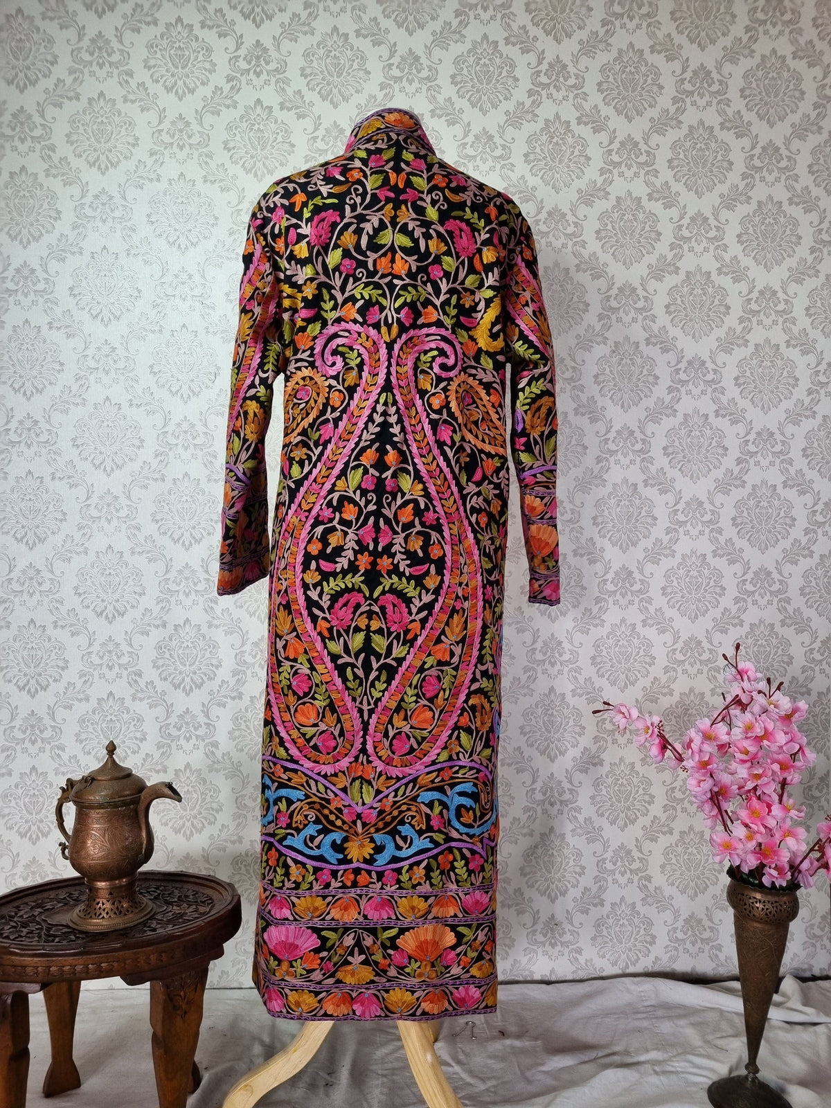 Full back view of a long black wool jacket with two large symmetrical pink-edged paisleys and colourful floral borders.