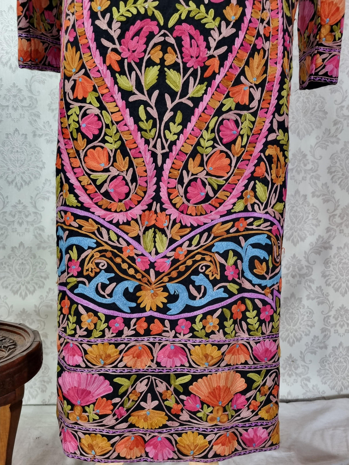 Lower back detail of the black jacket with bright floral vines, blue scrolling leaves and layered pink and orange hem borders.