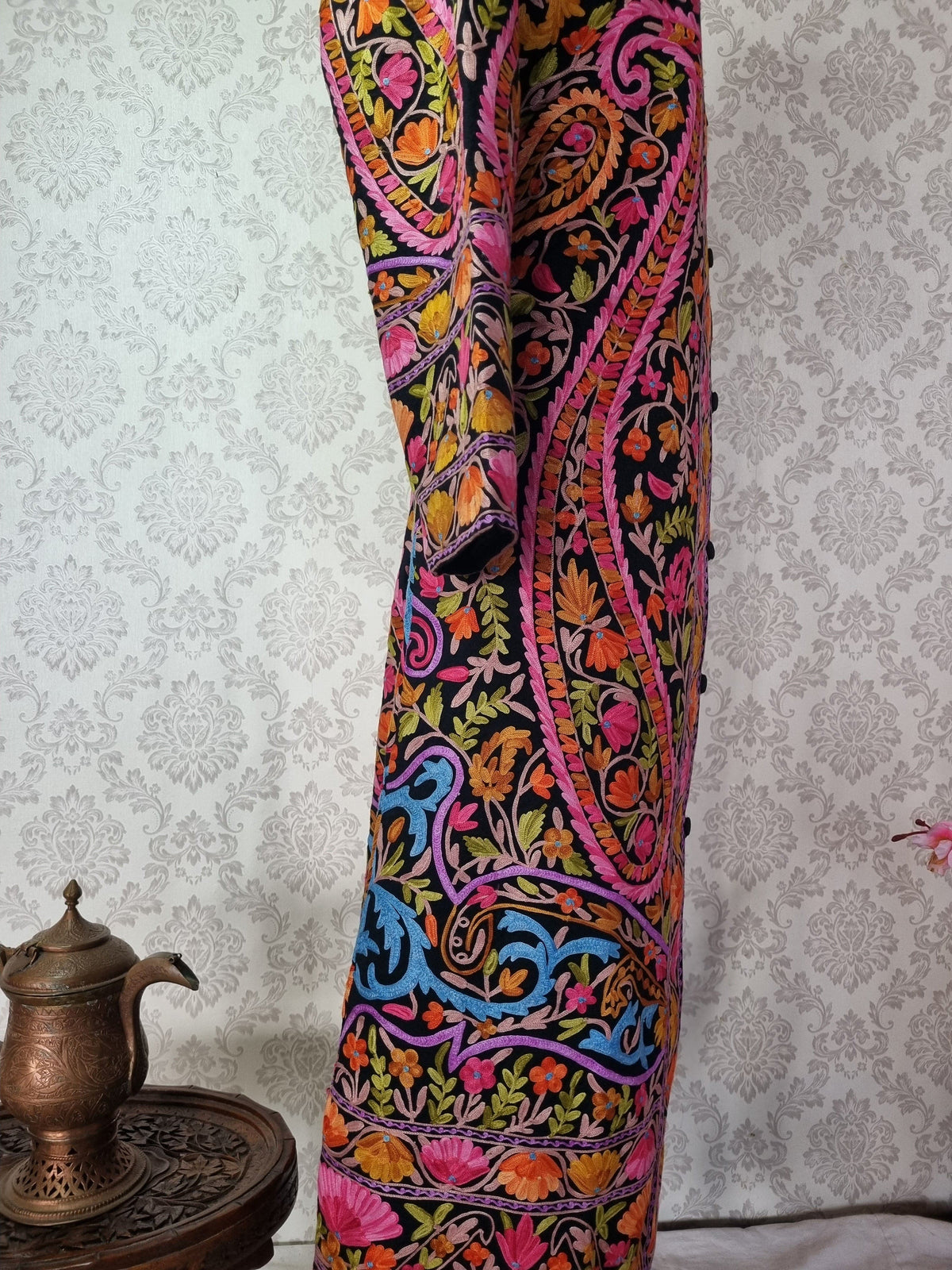 Side detail of the black jacket showing a large pink-edged paisley and multicoloured floral hem borders.