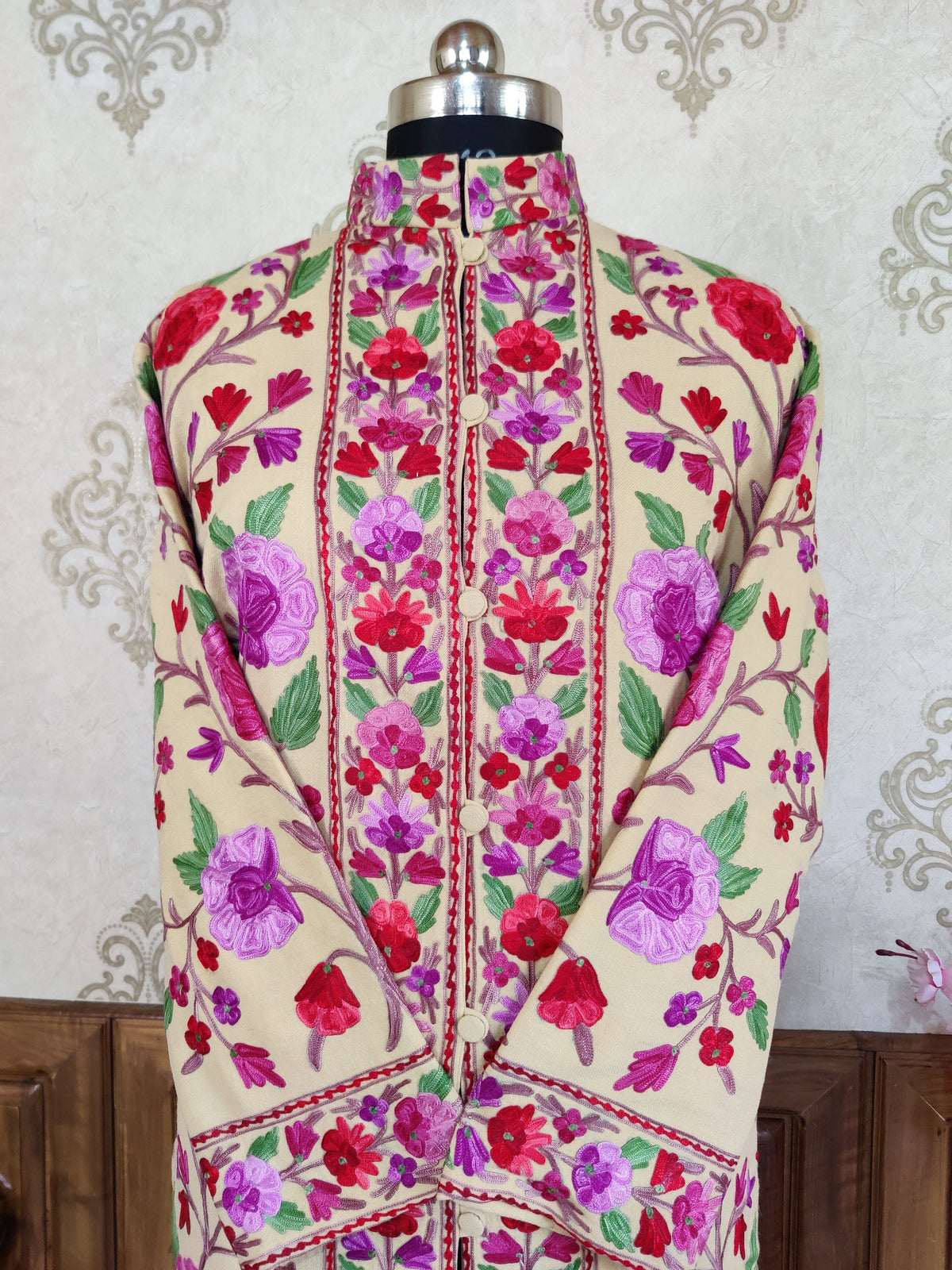 Upper front of a cream jacket with pink and purple Aari floral vines, green leaves, a stand collar and crossed sleeves