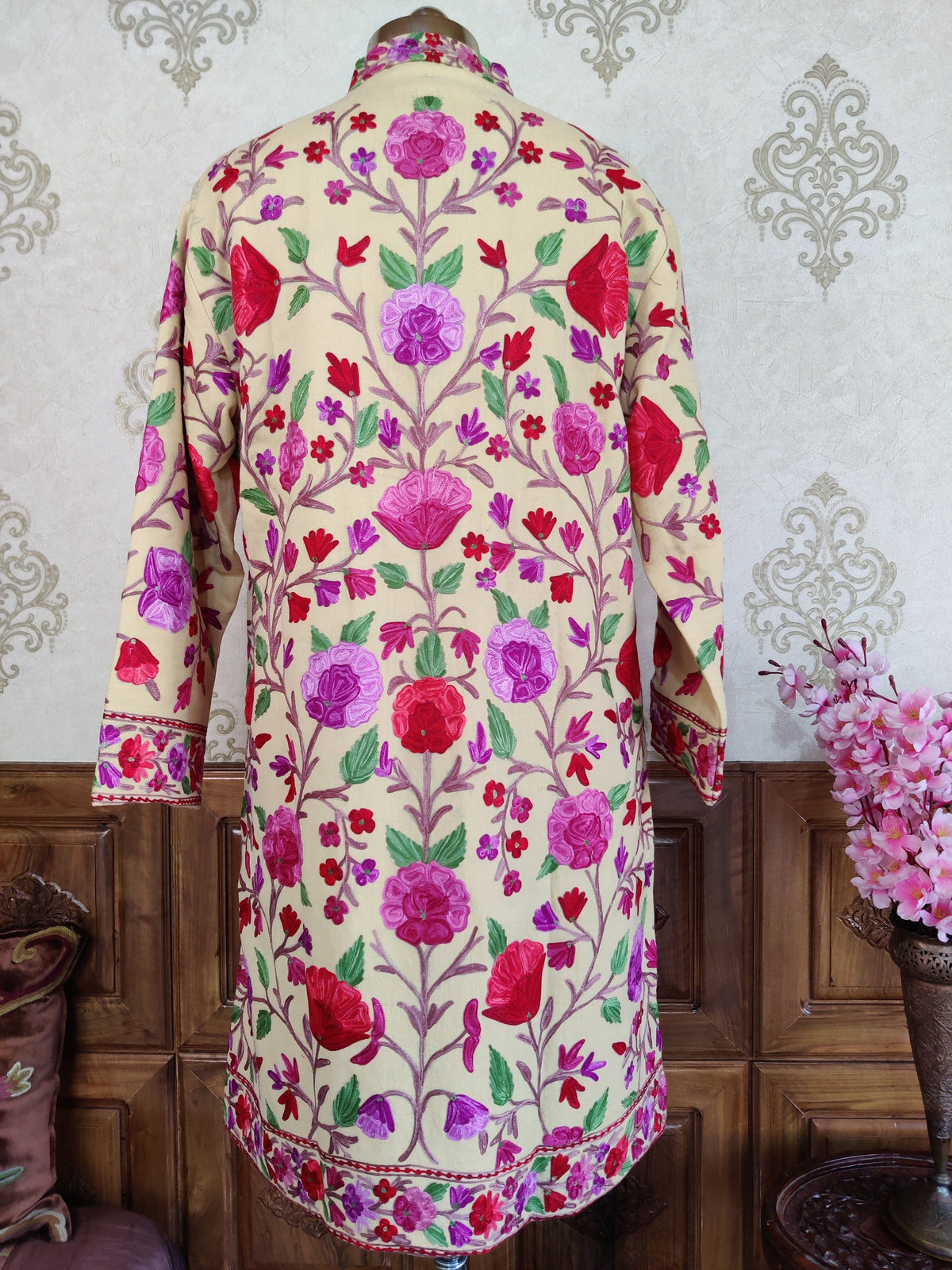 Back of a cream long jacket with symmetrical pink and purple Aari floral vines, green leaves and a narrow flowered hem border
