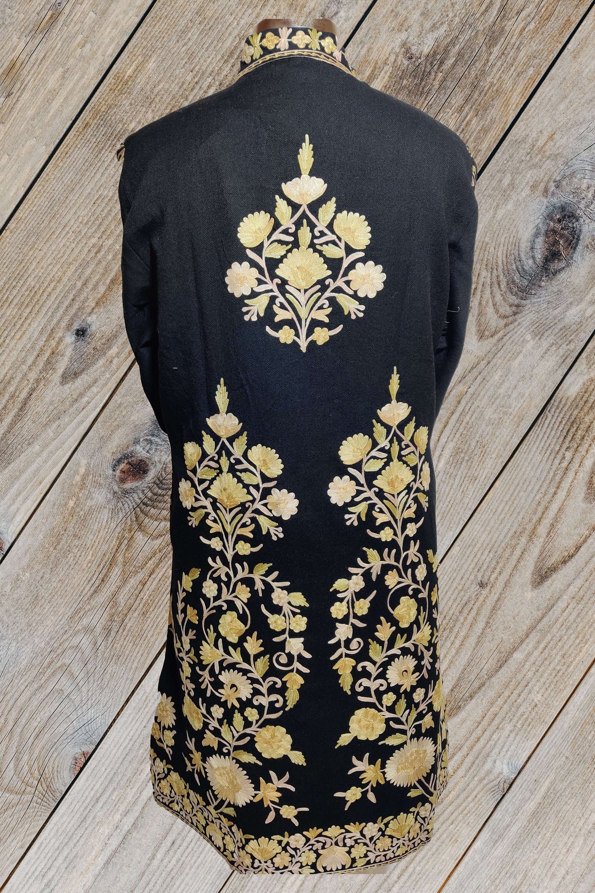 Back of a black long jacket, with a cream-and-yellow Aari floral medallion between the shoulders and tall floral sprays above the hem.