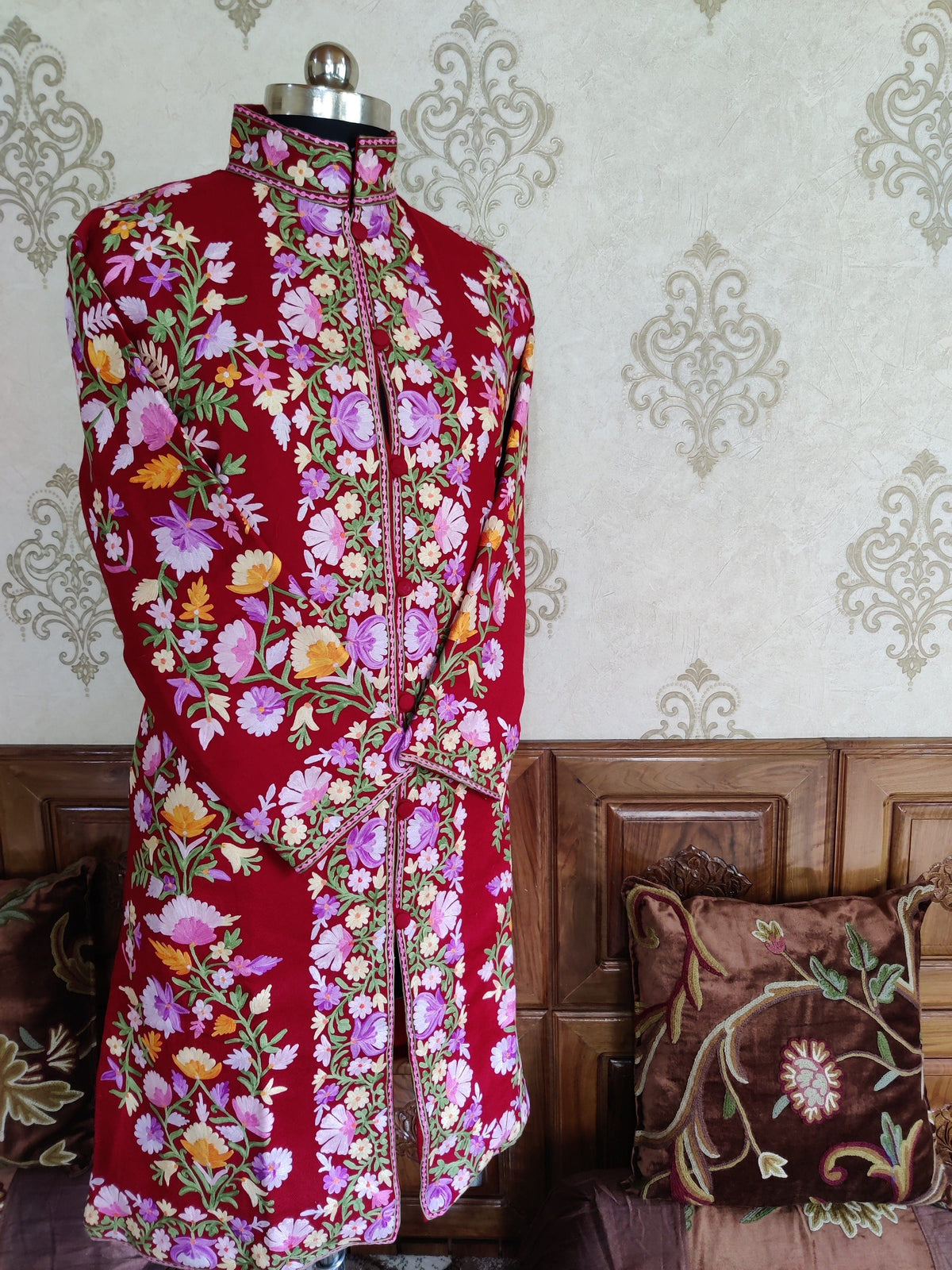 Maroon floral-embroidered jacket on a mannequin with crossed sleeves, showing borders along the front, cuffs and hem.