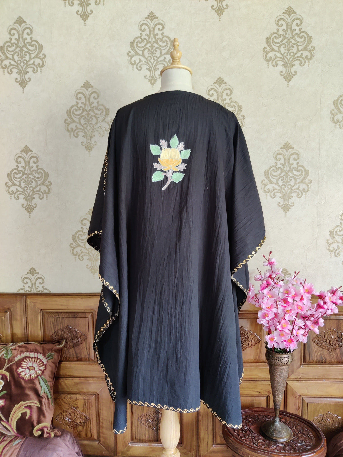 Back of a black kaftan with a small yellow-and-pink Aari floral motif between the shoulders and narrow embroidered edging
