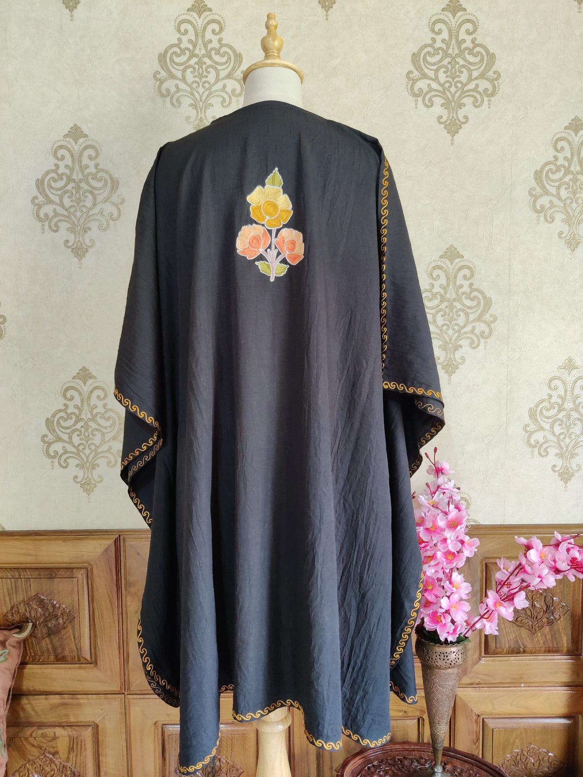 Back of a black kaftan with a small yellow and peach Aari bouquet high between the shoulders and narrow gold-toned edging