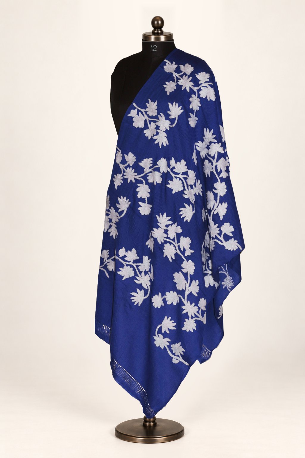 Blue merino wool stole draped over a mannequin’s shoulder, with large pale Aari flowers and curling leafy stems