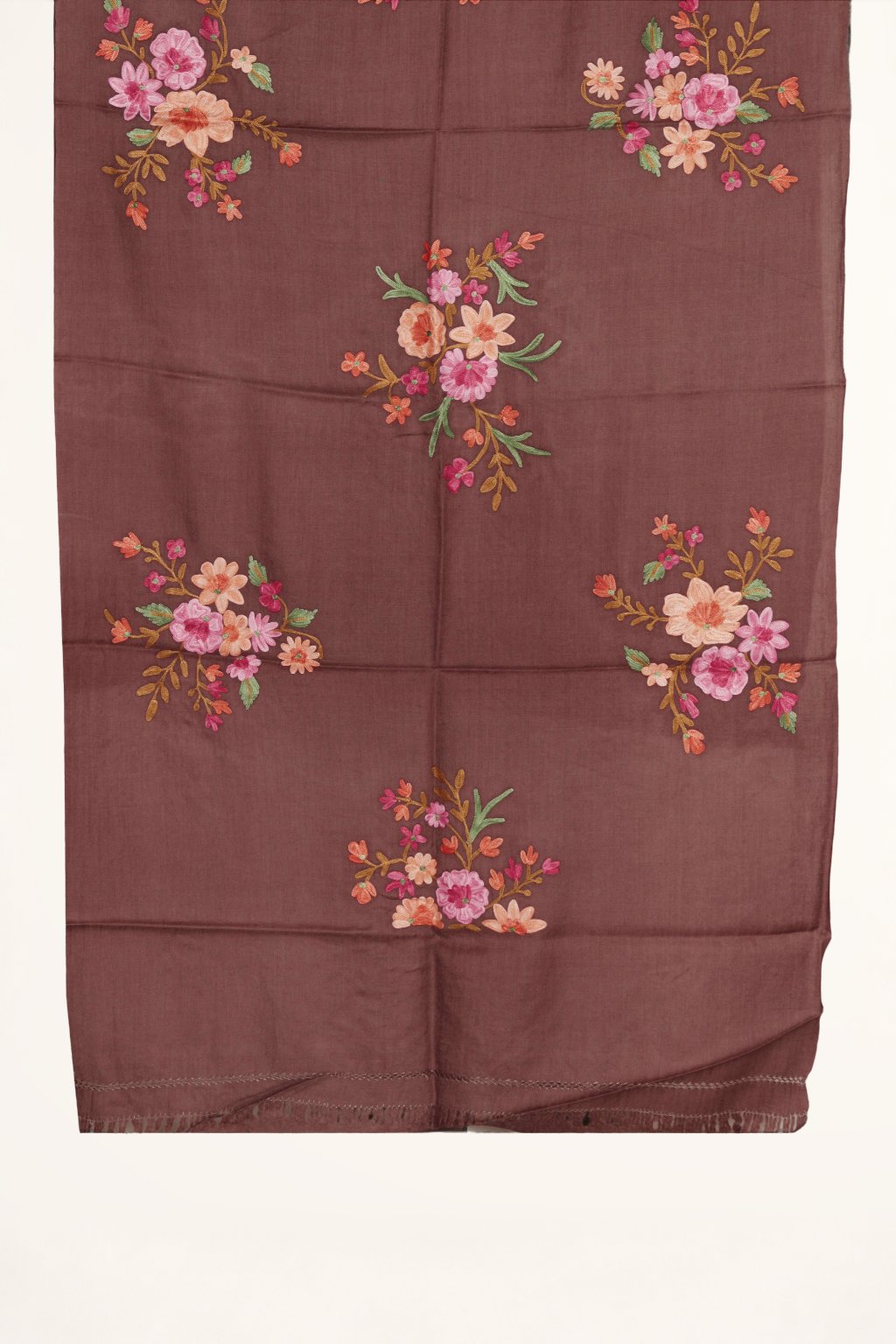 Brown merino wool stole laid flat on wooden boards, with scattered pink, peach and orange floral bouquets and a short fringe.