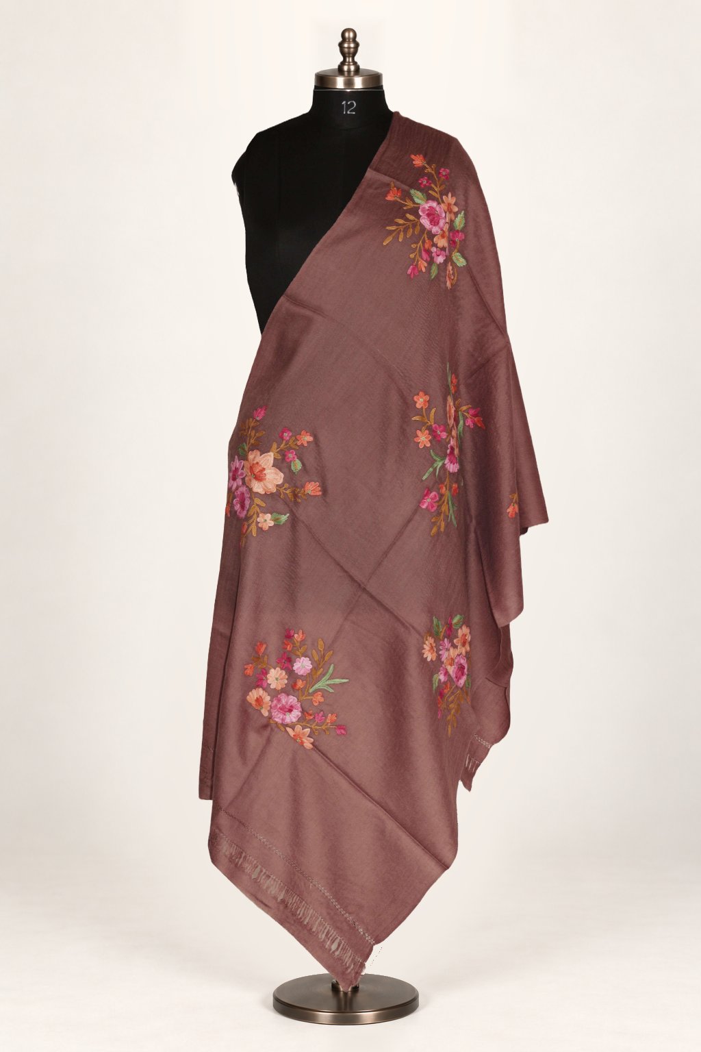 Brown merino wool stole draped over a mannequin’s shoulder, with scattered pink and orange Aari flower bouquets