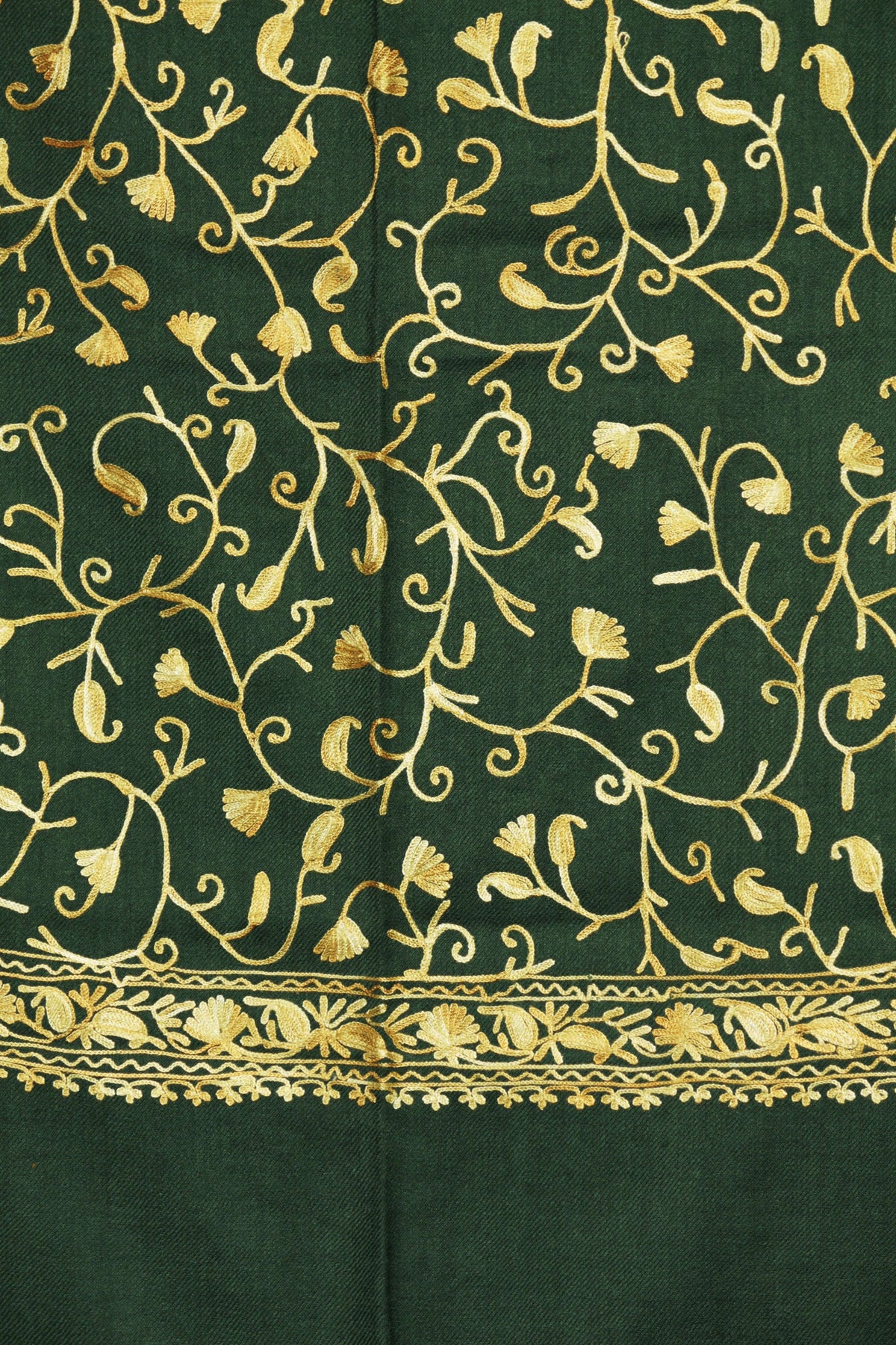Close-up of gold-toned Aari curling stems and small leaves on a green Merino wool stole, above a narrow embroidered border