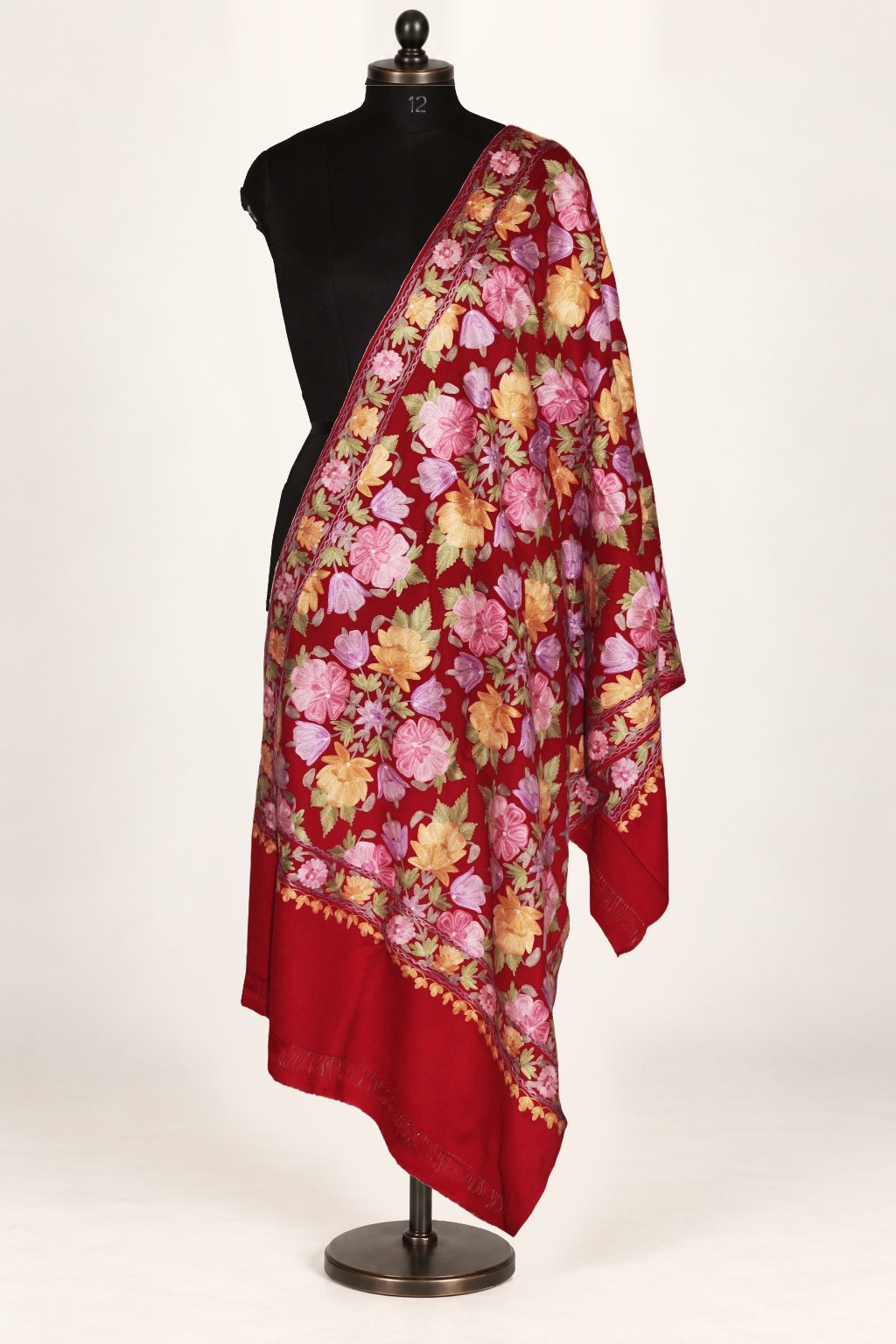 Red merino wool stole draped over a mannequin’s shoulder, with large pink and yellow Aari flowers and green leaves