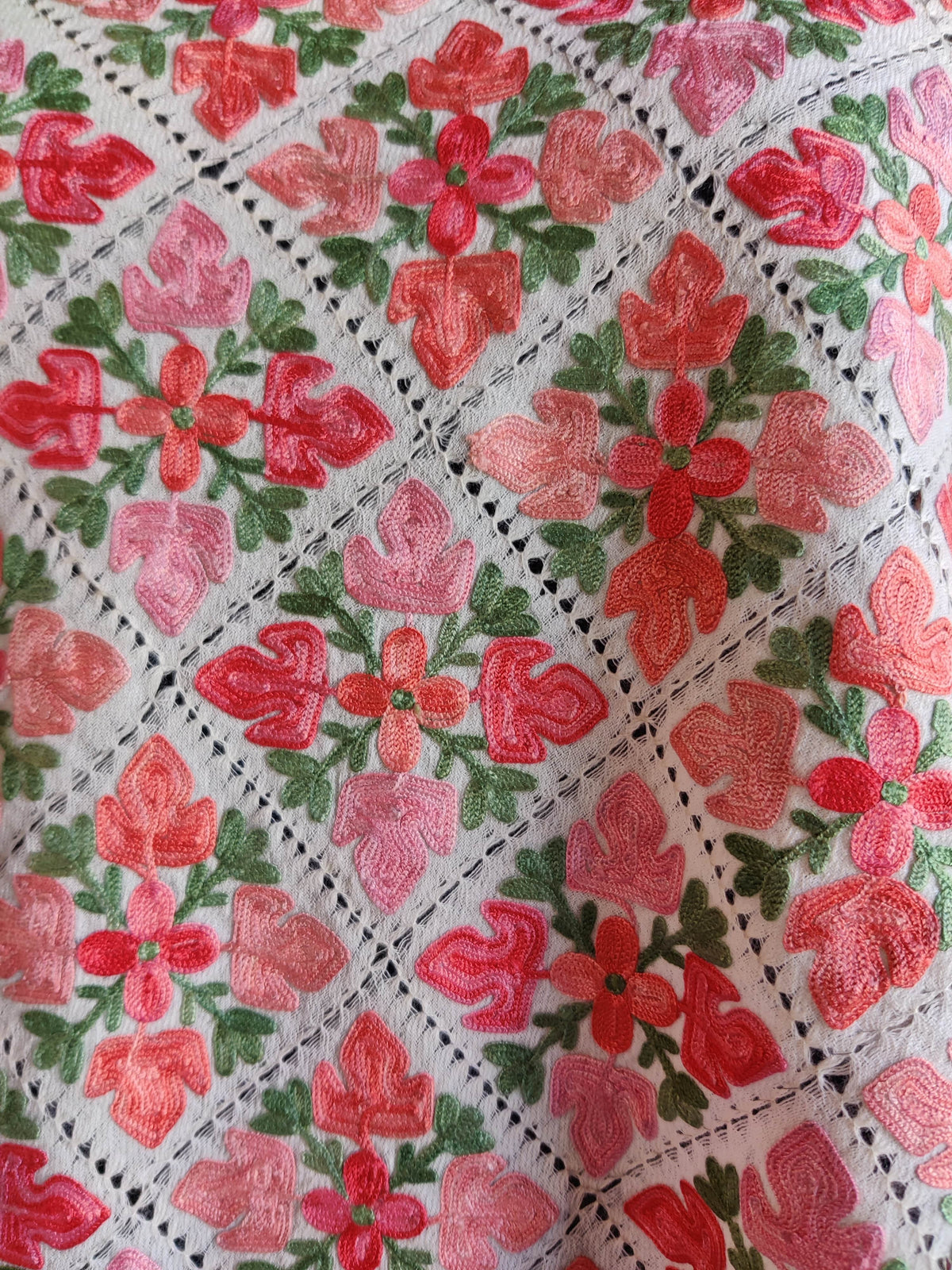 Close-up of pink and coral floral embroidery with green leaves inside the white stole’s diamond cutwork pattern.