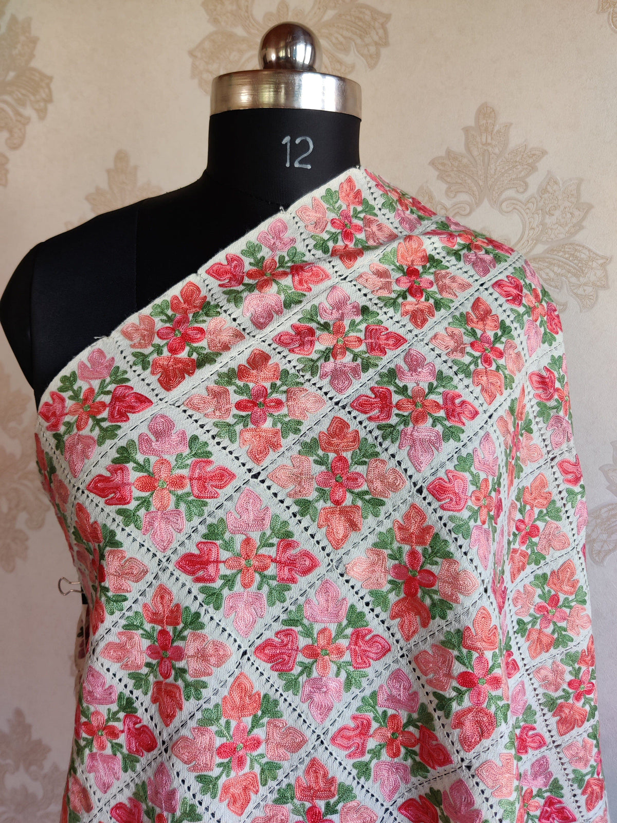 Upper draped view of the white stole with pink and coral flowers, green leaves and a diagonal openwork grid.