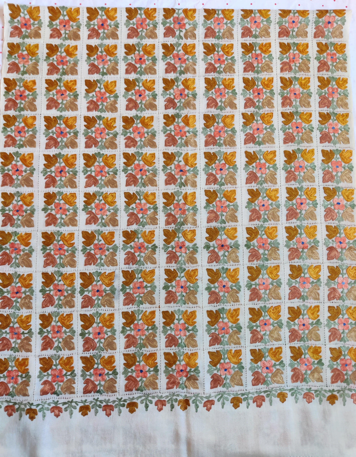 White Merino wool scarf spread flat, with a cutwork grid of colourful floral motifs above a plain white end