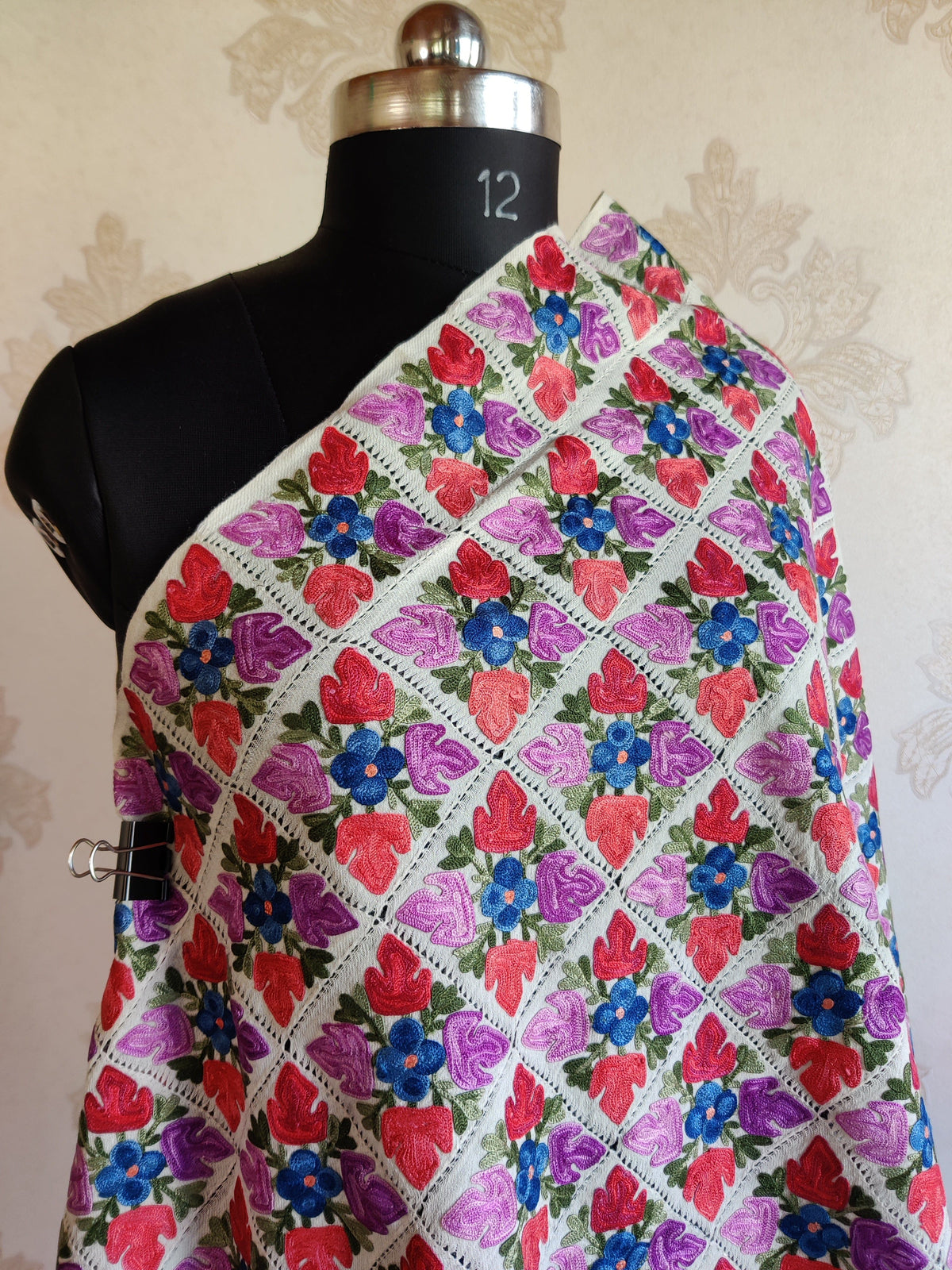White Merino wool stole across a mannequin's shoulder, showing colourful Aari floral diamonds and fine openwork divisions