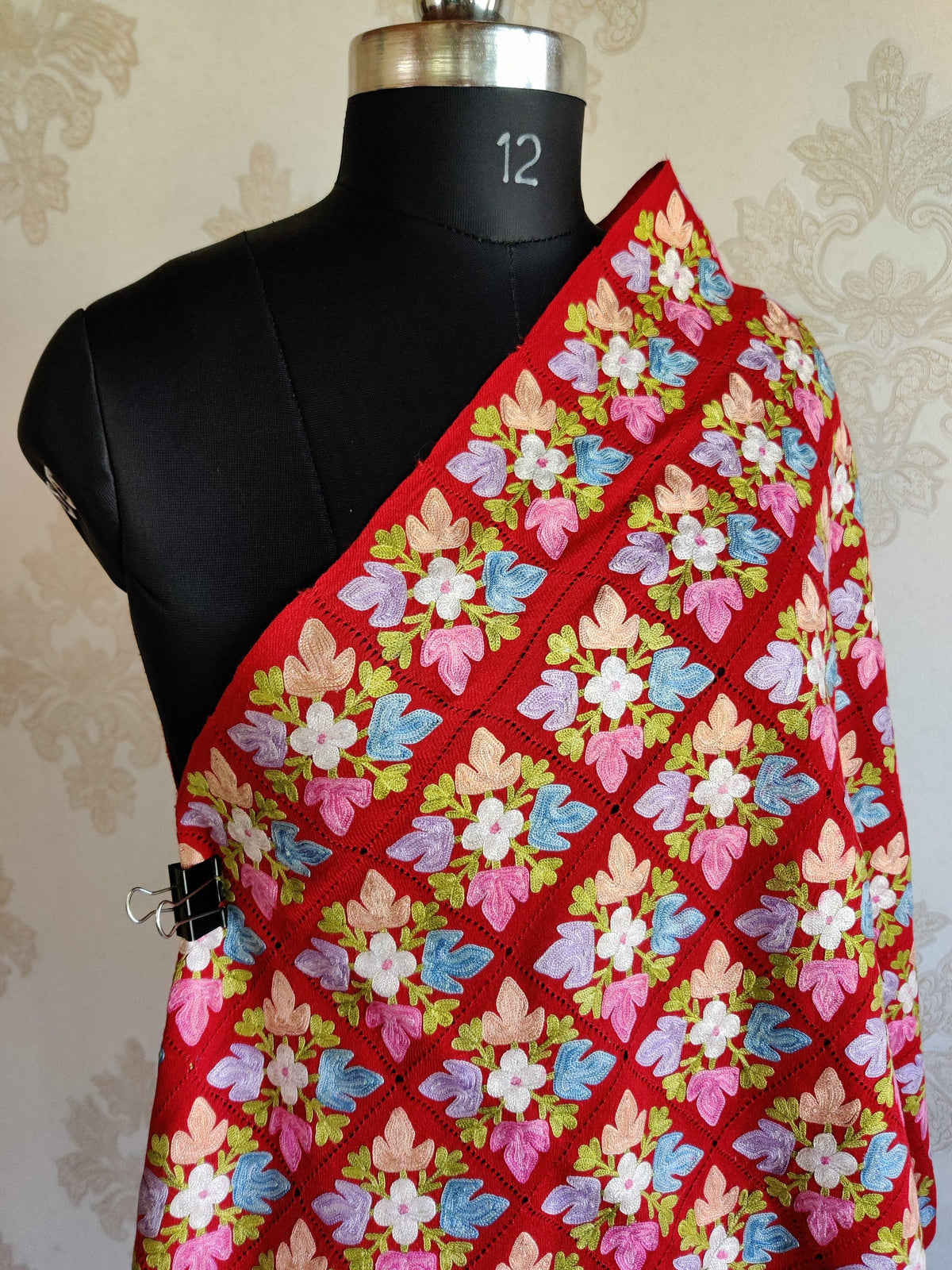 Upper draped view of the red stole with blue, pink, lavender and ivory flowers and green leaves.