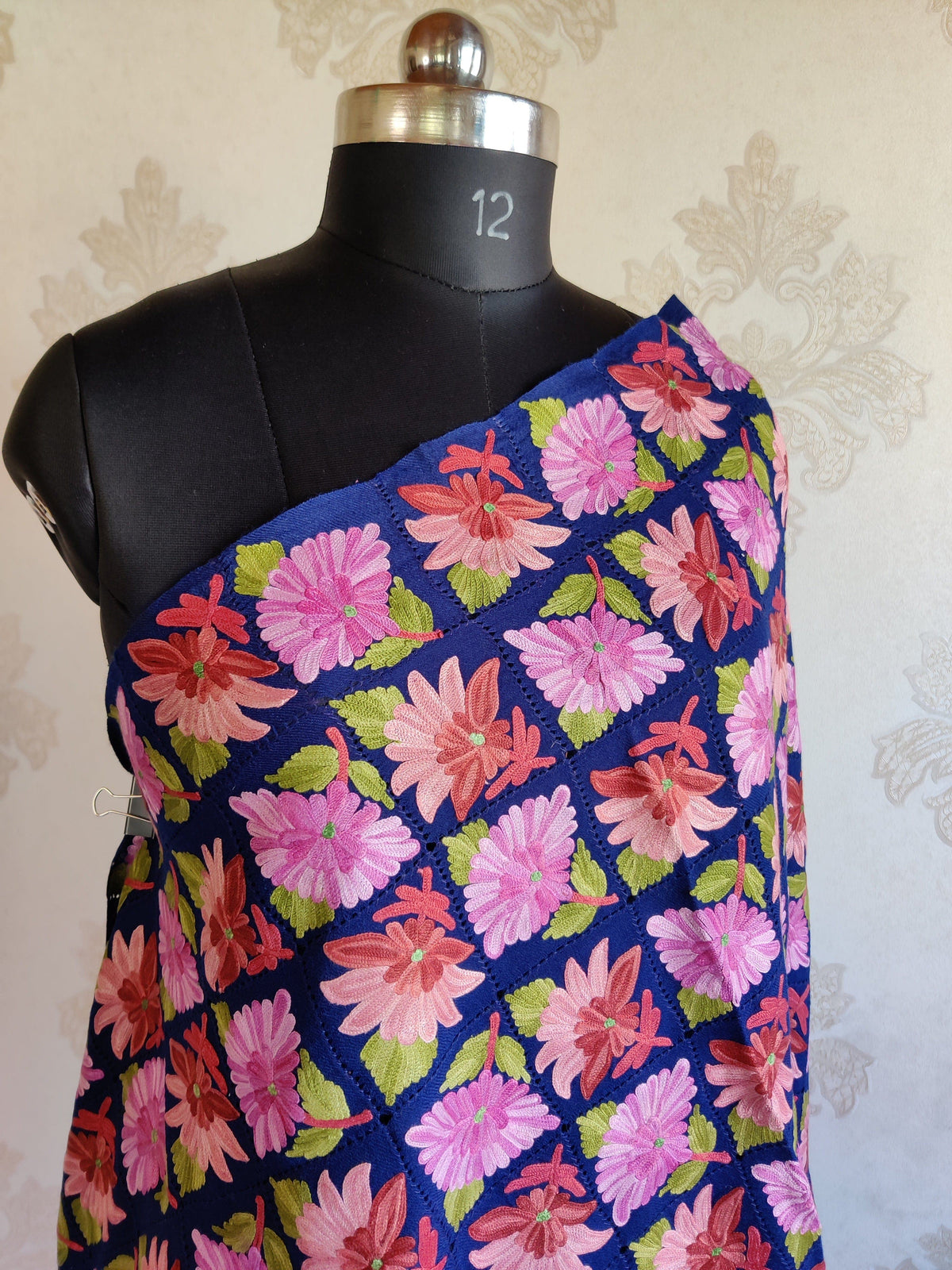Angled upper view of royal-blue Merino wool scarf showing rows of pink Aari flowers and green leaves