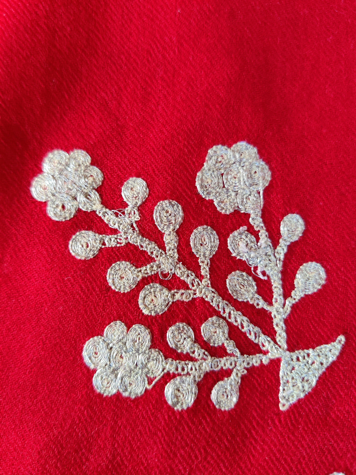 Close-up of a silver-toned Tilla flowering sprig on plain red Merino wool scarf fabric
