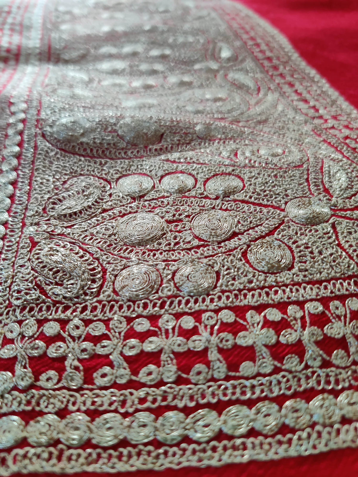 Angled macro view of pale metallic Tilla threadwork in the paisley and floral border of a red Merino wool stole