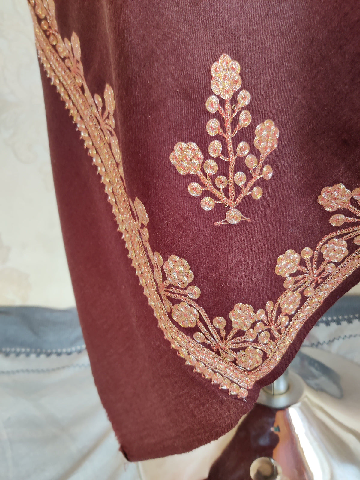 Hanging corner of a brown Merino wool stole with a gold-toned Tilla floral sprig above a matching flowered border