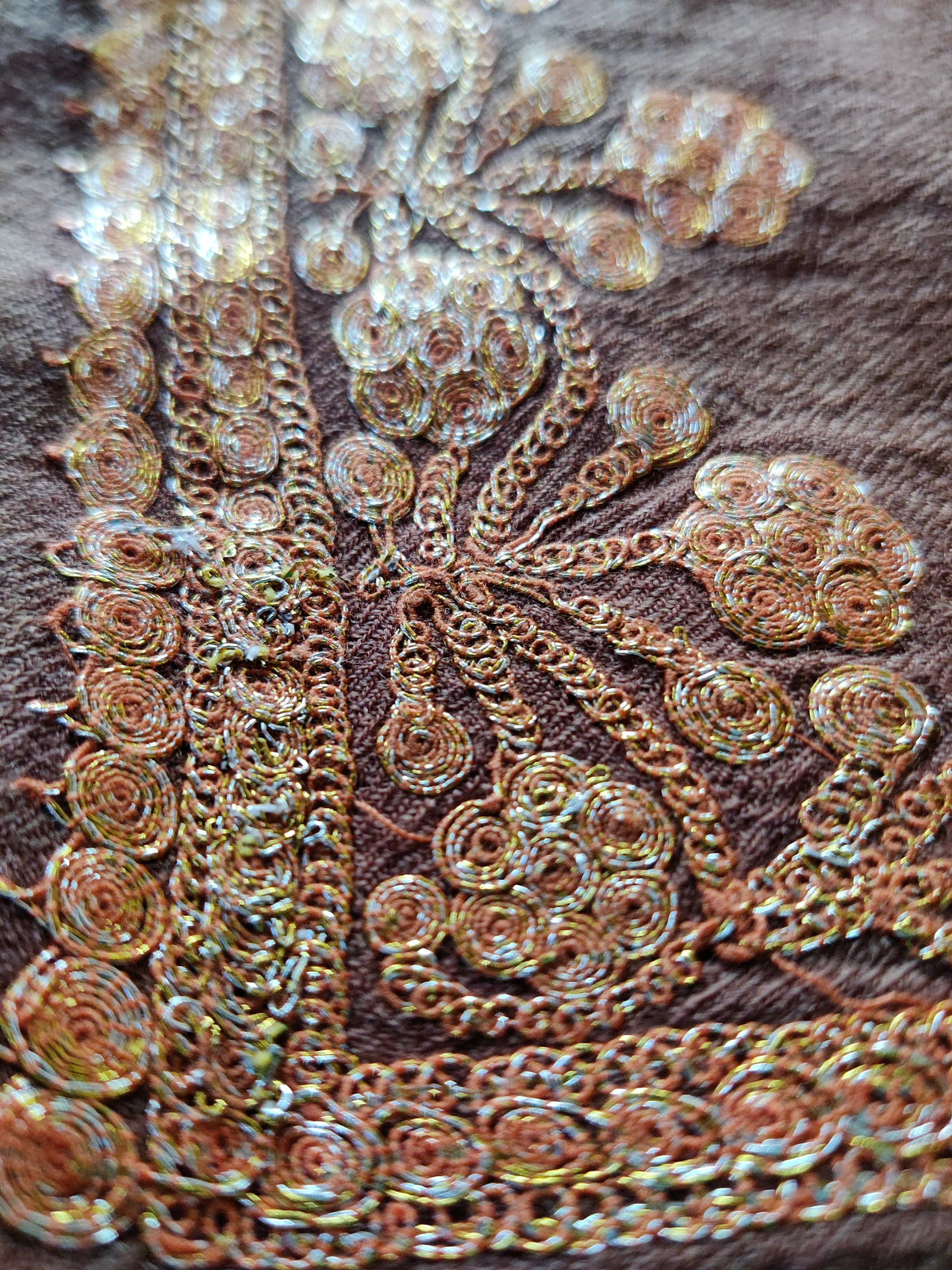 Macro view of gold-toned Tilla threadwork forming small flowers and round leaves along the brown Merino wool stole border