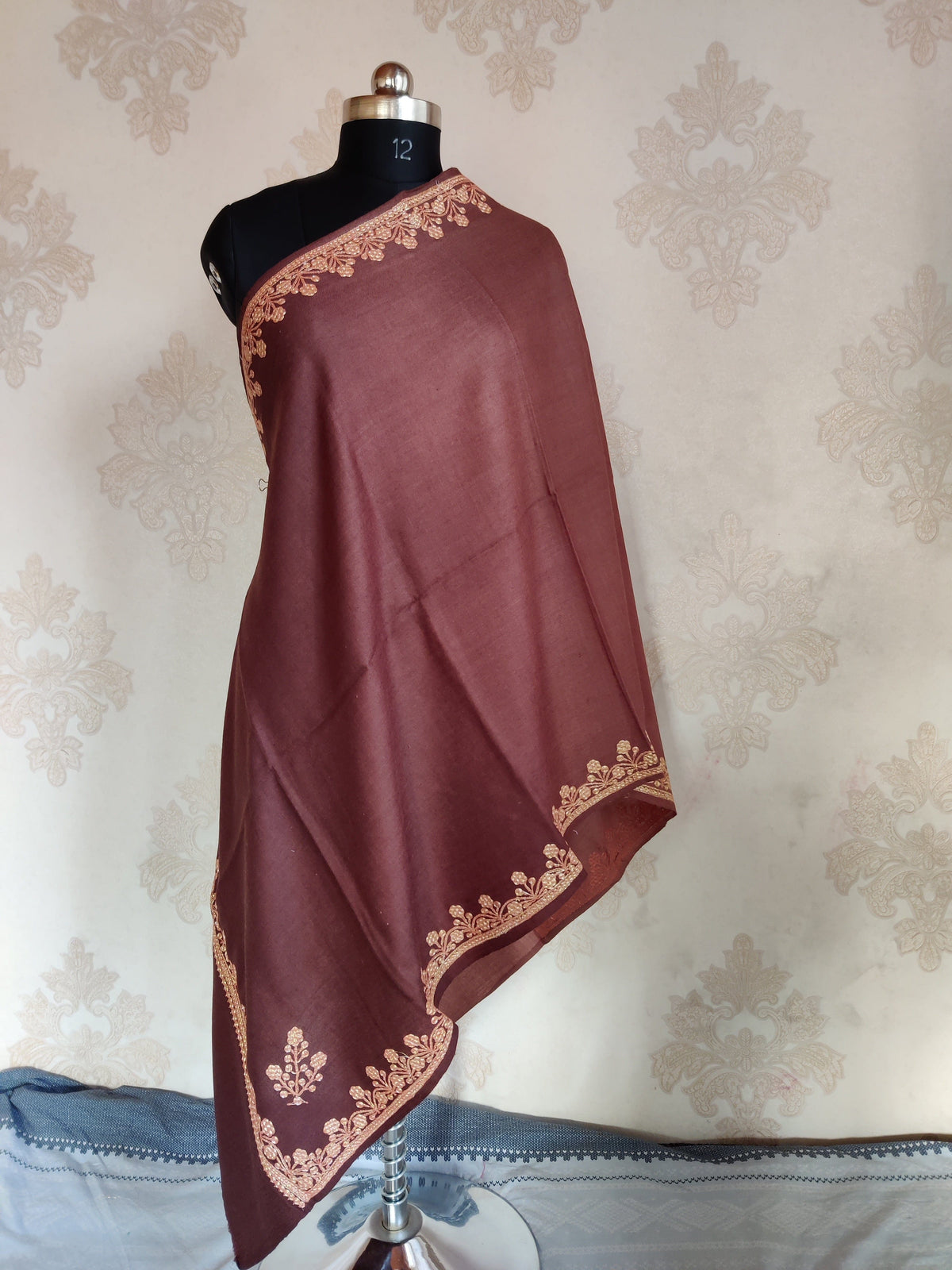 Brown Merino wool stole draped on a mannequin, with a gold-toned Tilla floral border and small corner sprigs