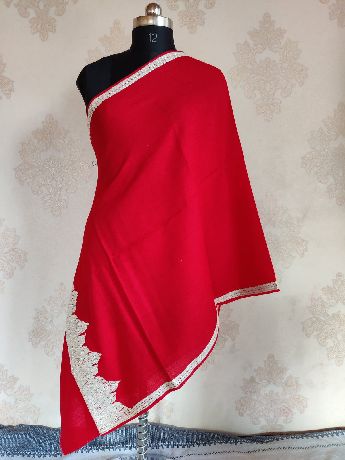 Red merino wool stole draped on a mannequin, with pale Tilla paisleys at one end and narrow embroidered borders