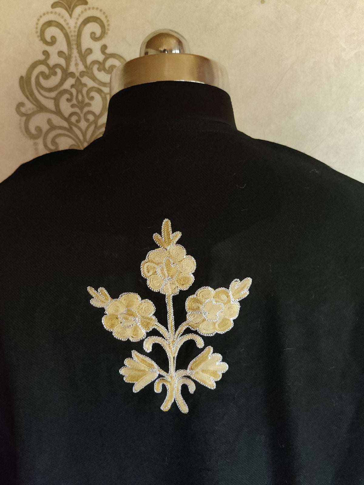 Back-neck detail of a black pheran with a small pale-gold three-flower sprig beneath the neckline.