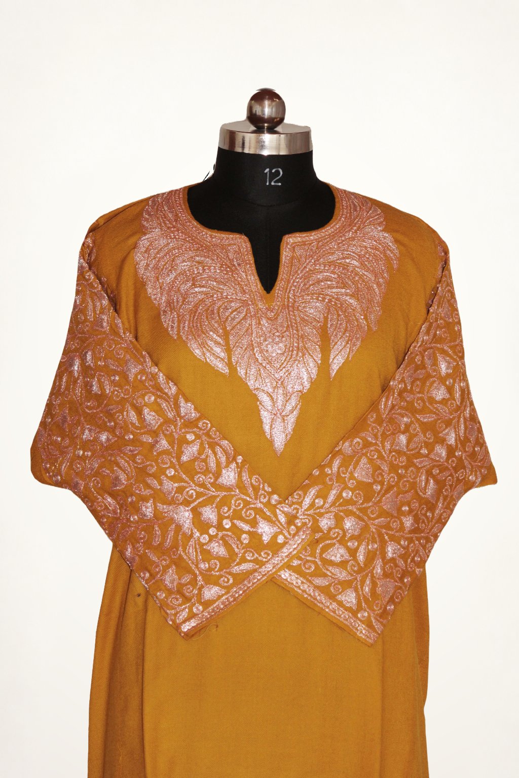 Front view of mustard pheran with sleeves crossed, showing pale pink Tilla embroidery around the split neckline and sleeves